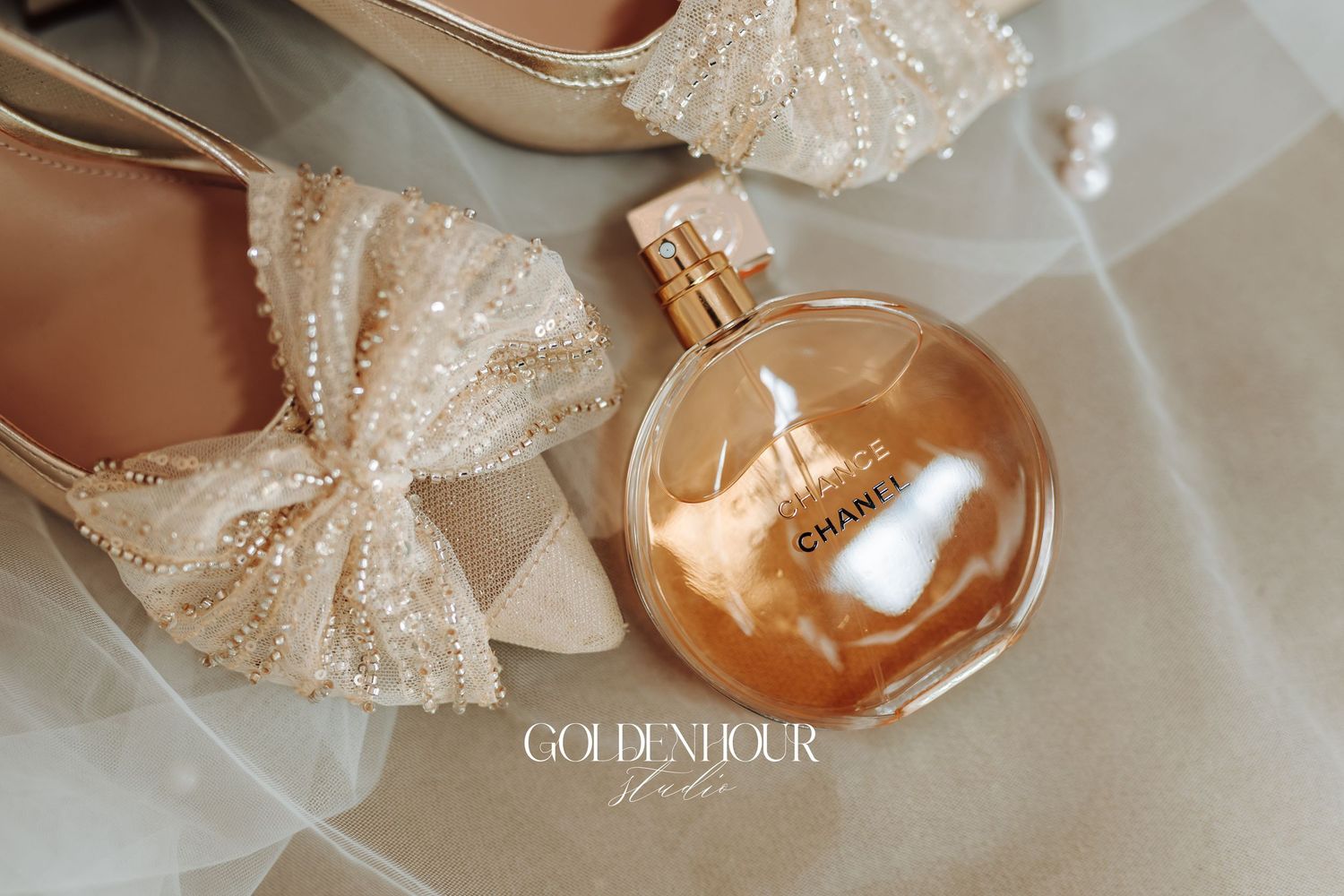 Elegant bridal accessories including champagne-colored heels, perfume bottles, and delicate lace details arranged on white fabric.