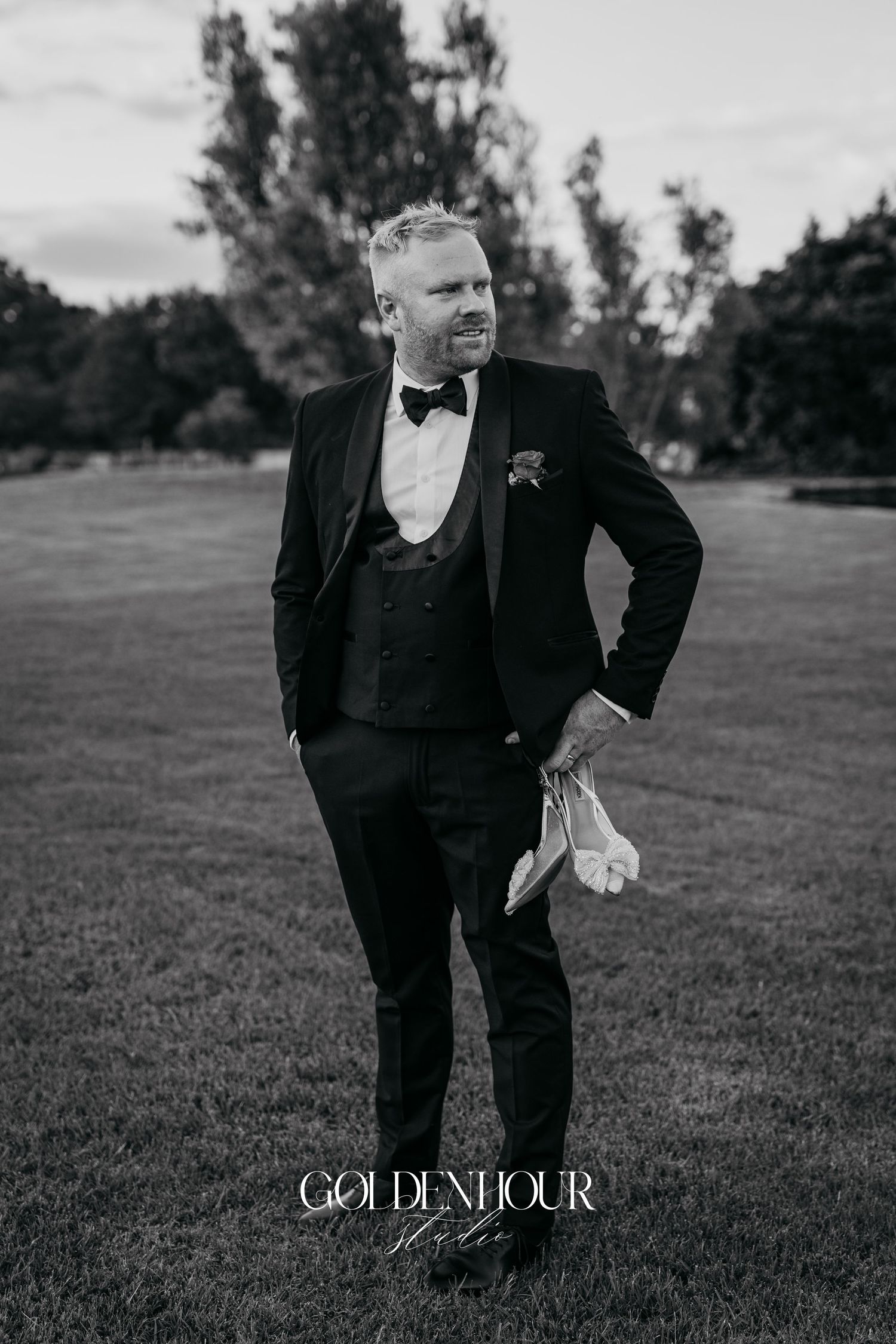 Black and white photo series showing person in formal tuxedo suit posing playfully on grassy field outdoors.