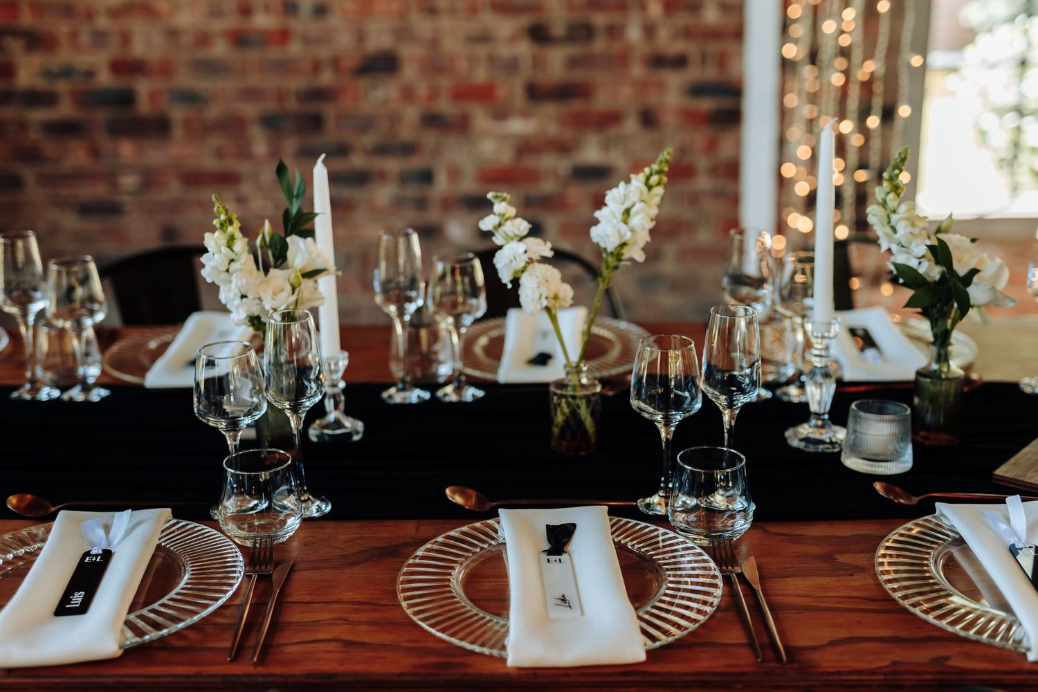 Elegant table settings with wine glasses and place cards line a rustic brick wall at an upscale restaurant.