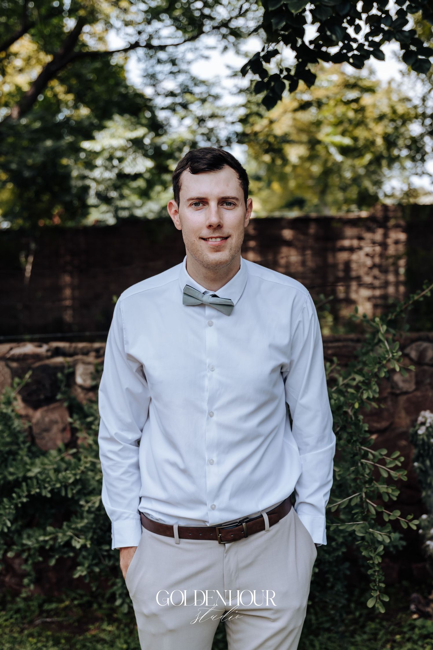 Wedding attire featuring light khaki pants, white dress shirt, and bow tie in an outdoor garden setting.