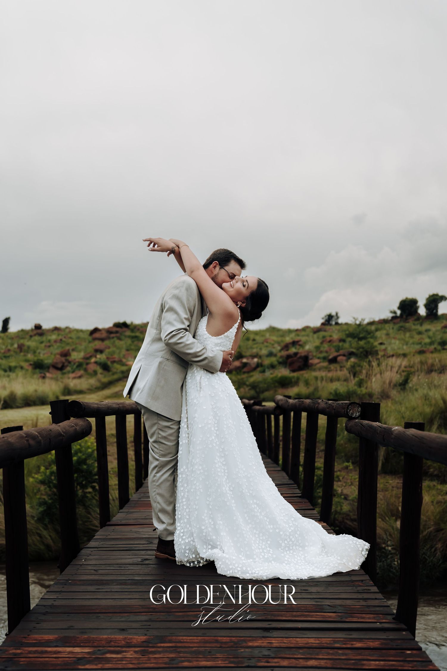 Newlyweds share an intimate dance pose on a wooden boardwalk surrounded by natural landscape.