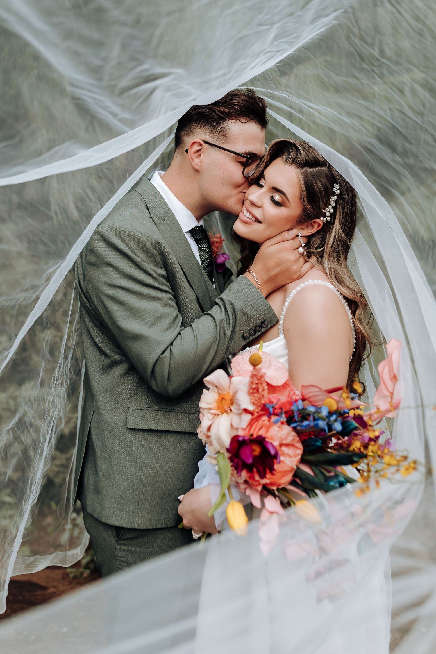 A romantic wedding moment with a flowing veil and colorful floral bouquet featuring orange and purple blooms.