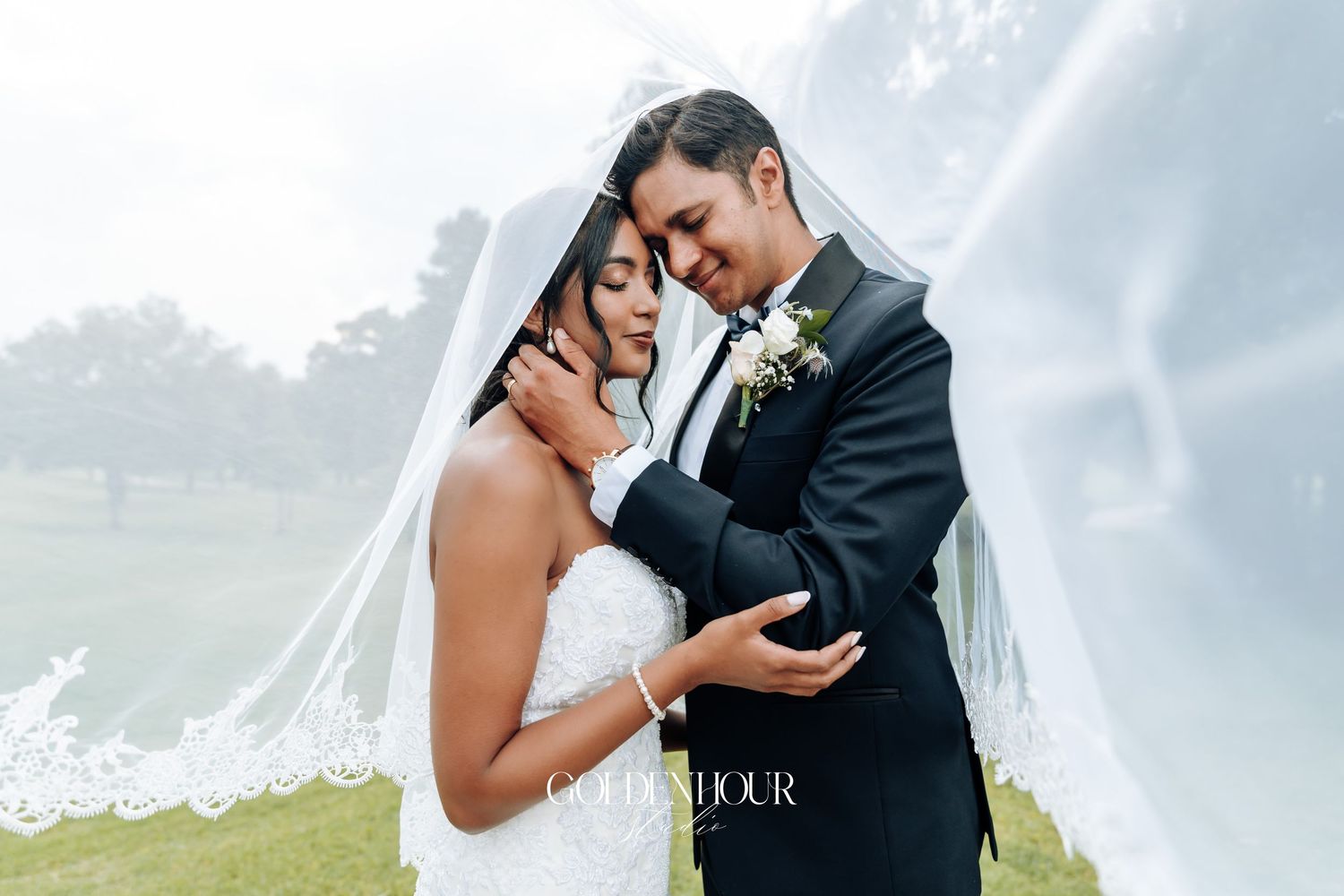 Intimate wedding portrait captured against cloudy sky with flowing veil.