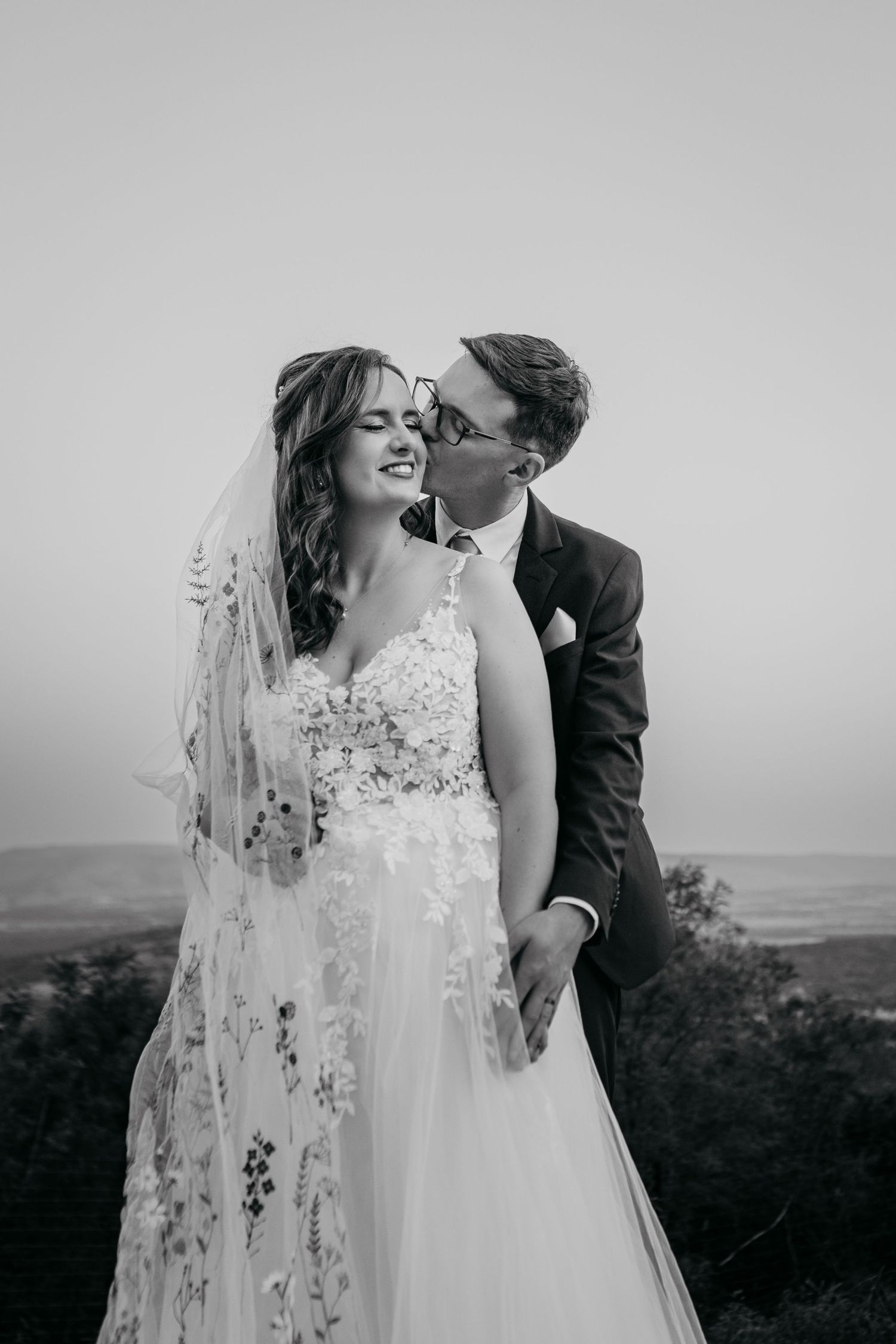 A romantic black and white wedding portrait series showing tender moments between newlyweds against a scenic landscape.