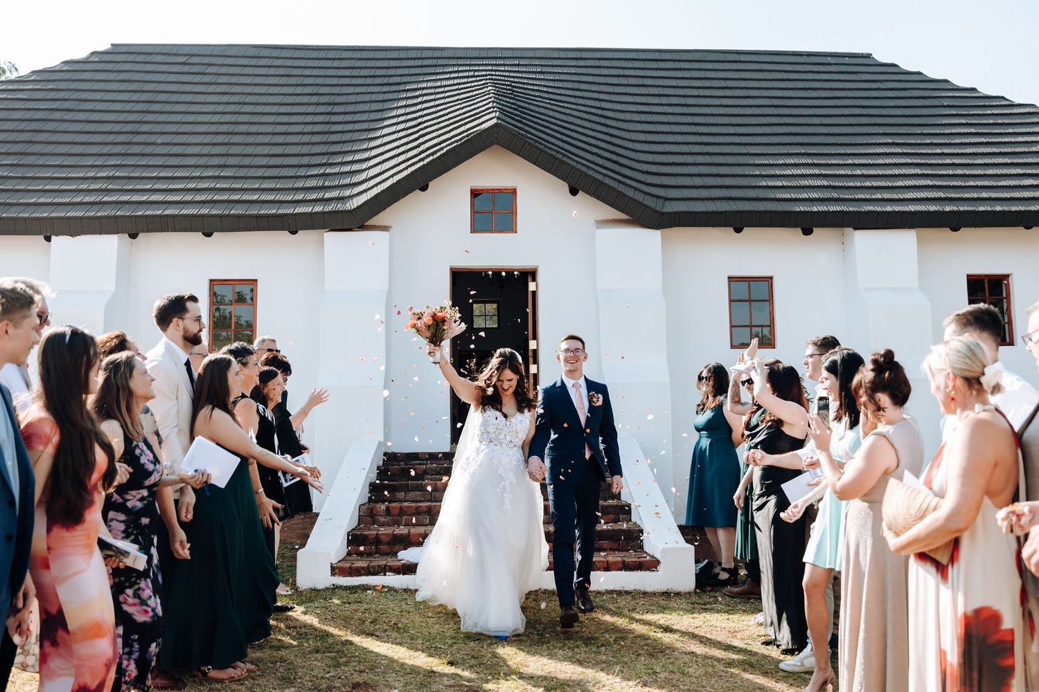 Wedding guests line up outside a white building to celebrate with the newlyweds.