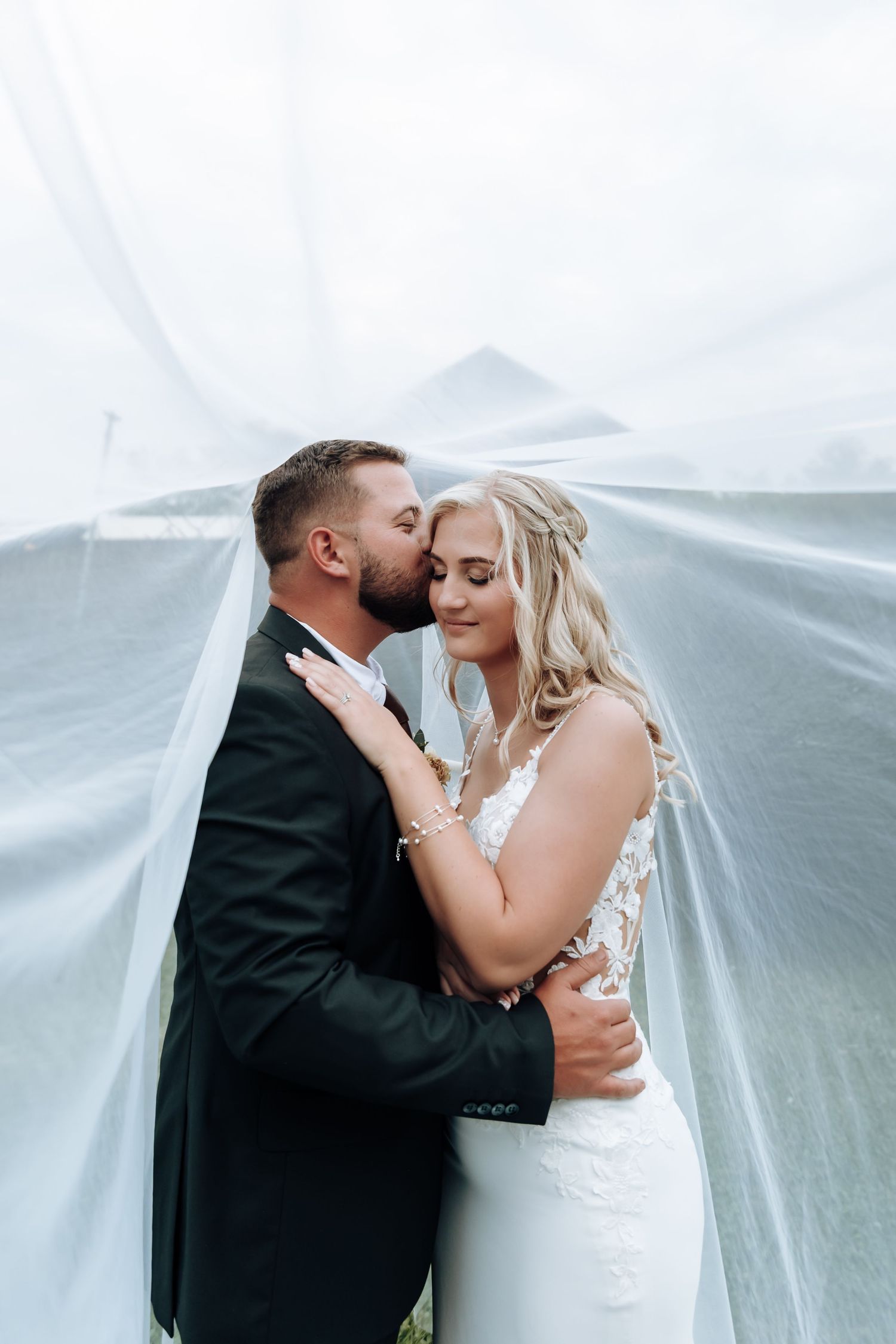 Romantic wedding couple shares intimate moments under flowing white veil in series of artistic photos.