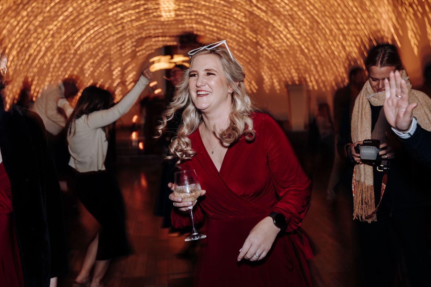 Woman in red dress dancing joyfully at elegant party with warm string lights glowing in background.