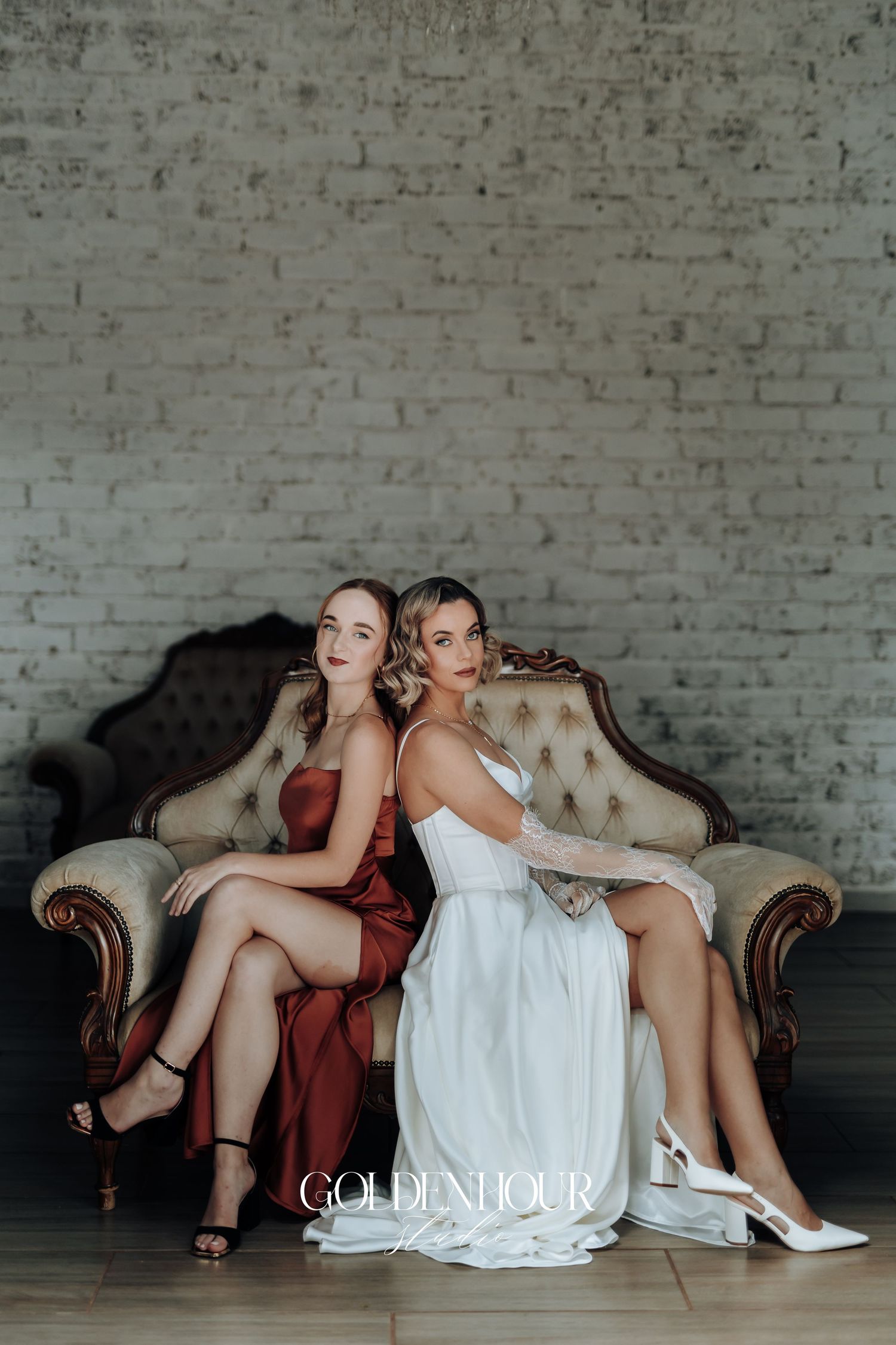 Bridesmaids in white and burgundy dresses lounge on antique sofa during photoshoot.