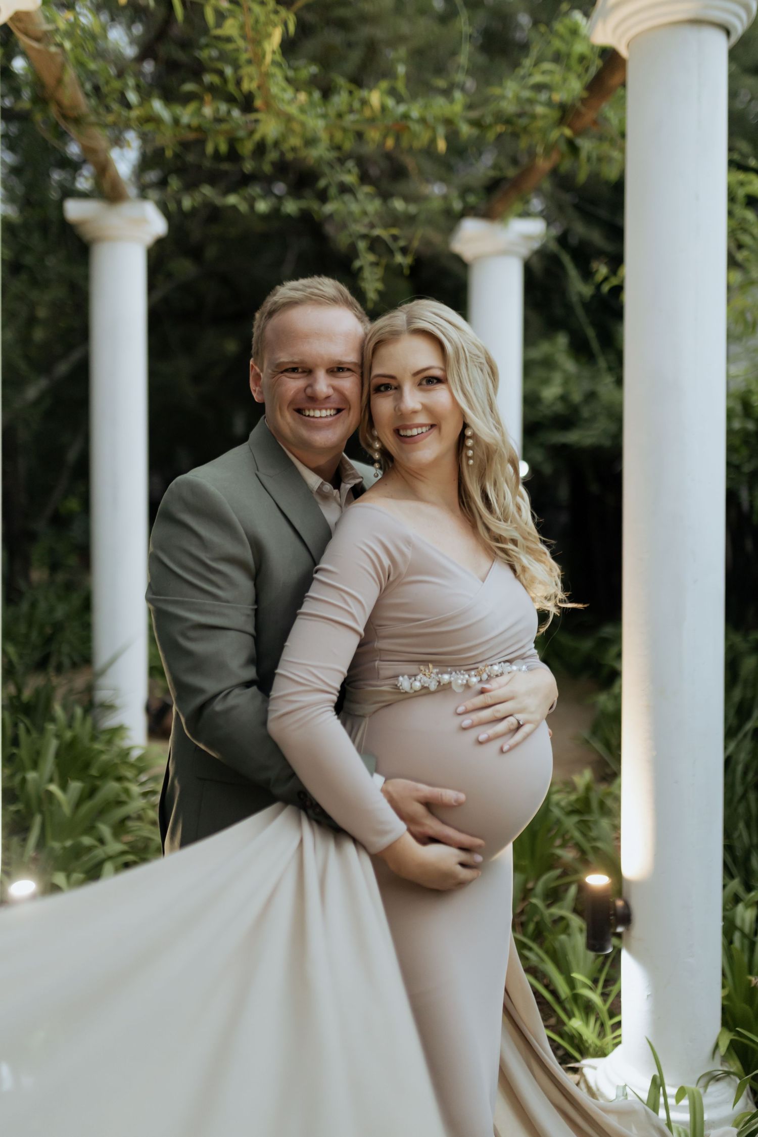 A joyful maternity session featuring a couple posing between elegant white columns.