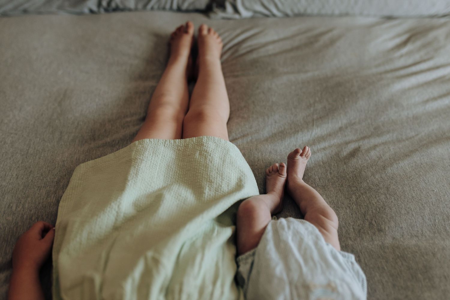 A series of feet poking out from under cozy white bedding while lying in bed.