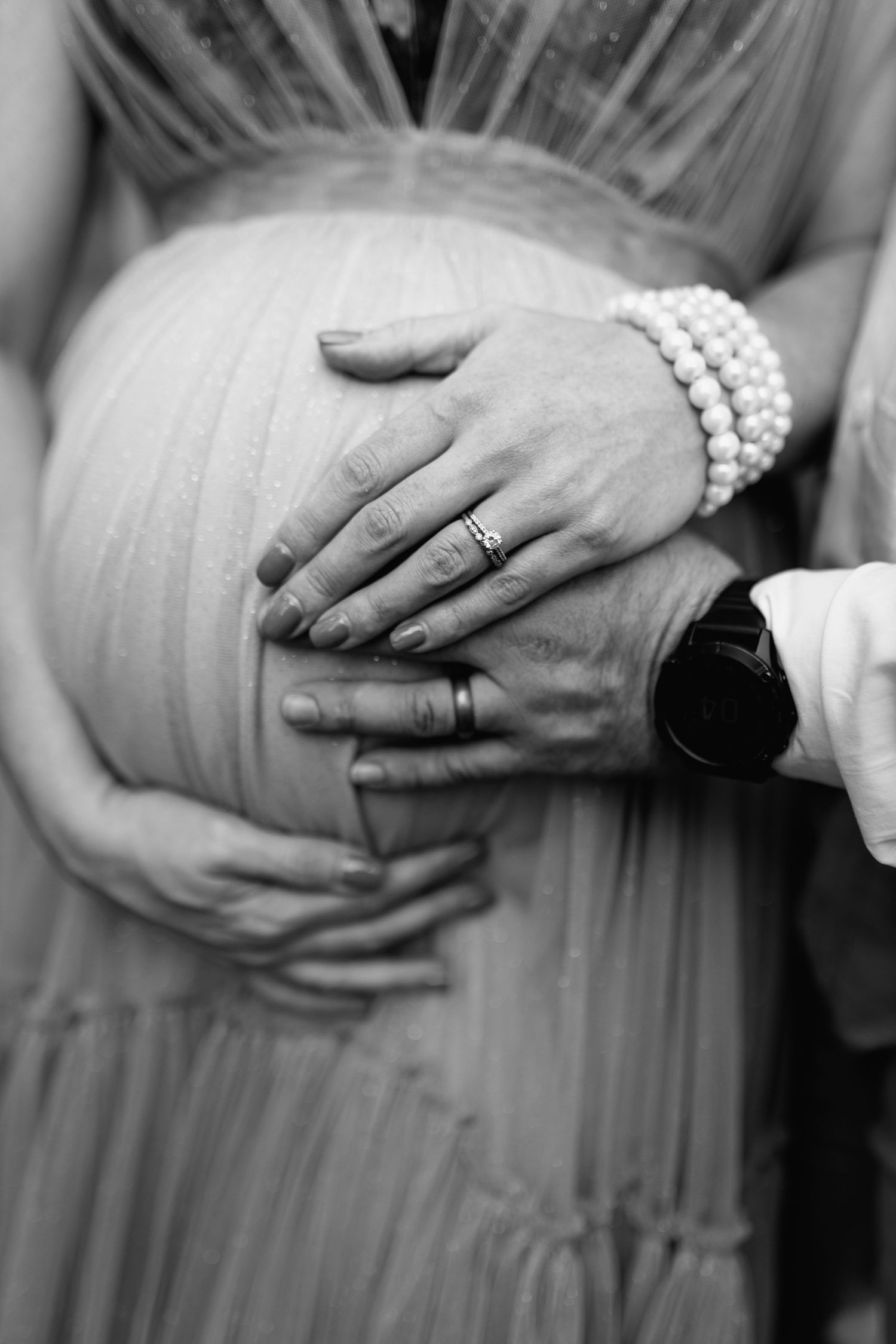 Black and white close-up shots showing hands with pearl bracelet and wedding ring resting on a pregnant belly.