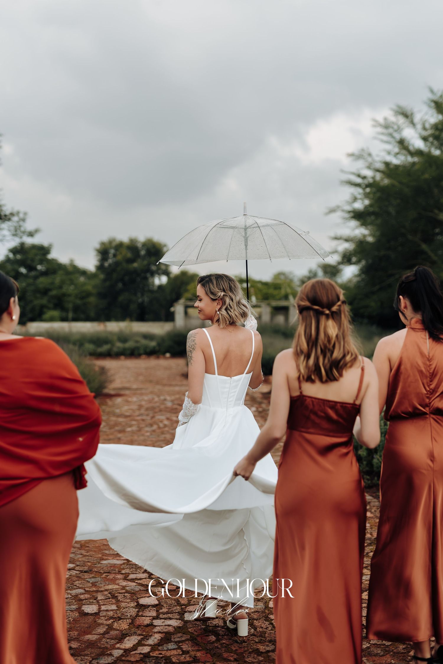 Bride in white dress with bridesmaids in rust-colored dresses pose outdoors.