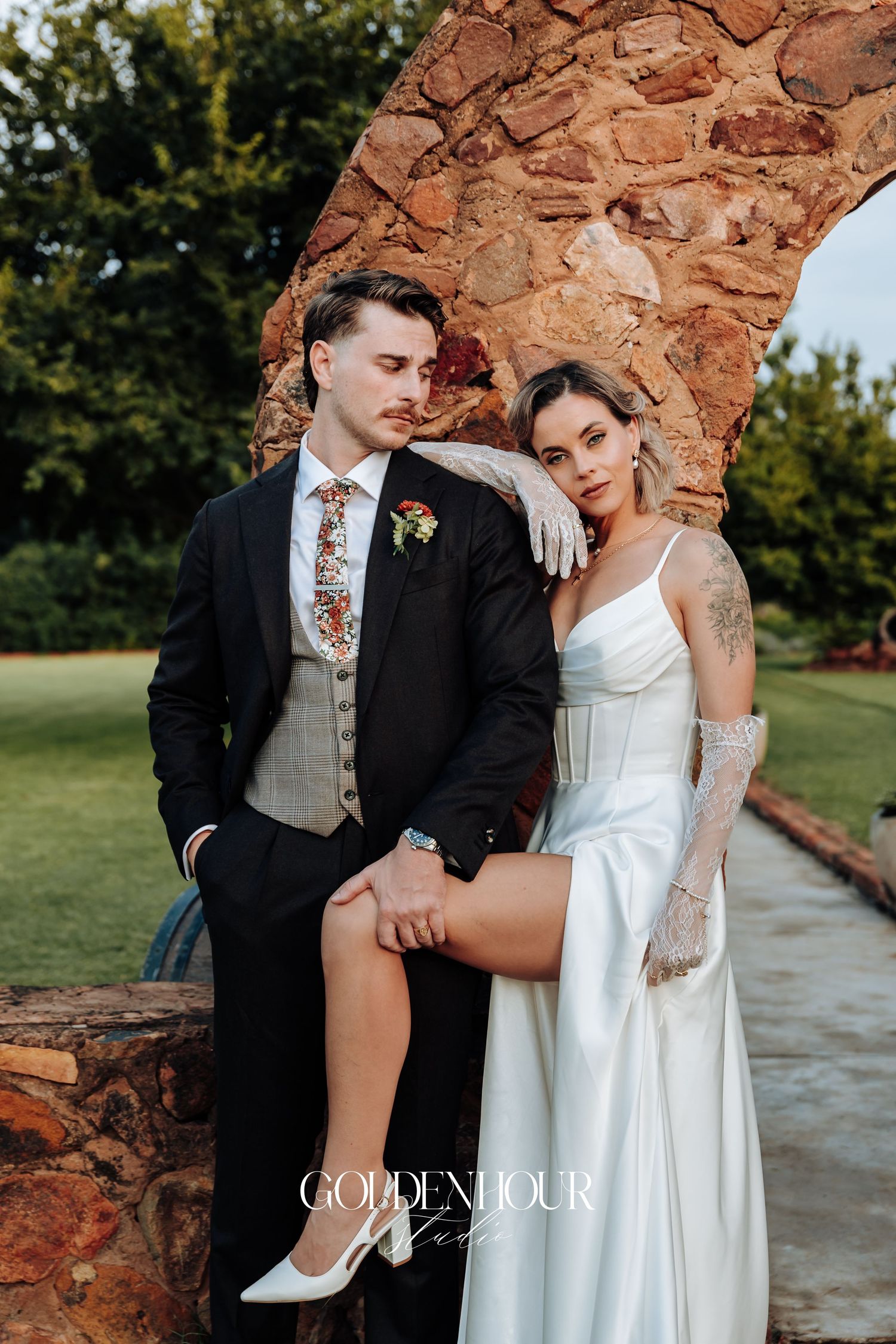 Wedding couple posing against rustic stone wall outdoors.