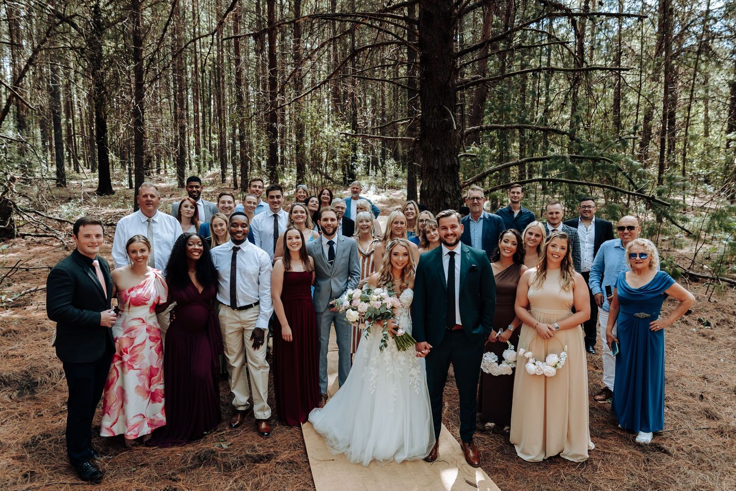 Wedding party poses together in a scenic forest setting during an outdoor ceremony celebration.