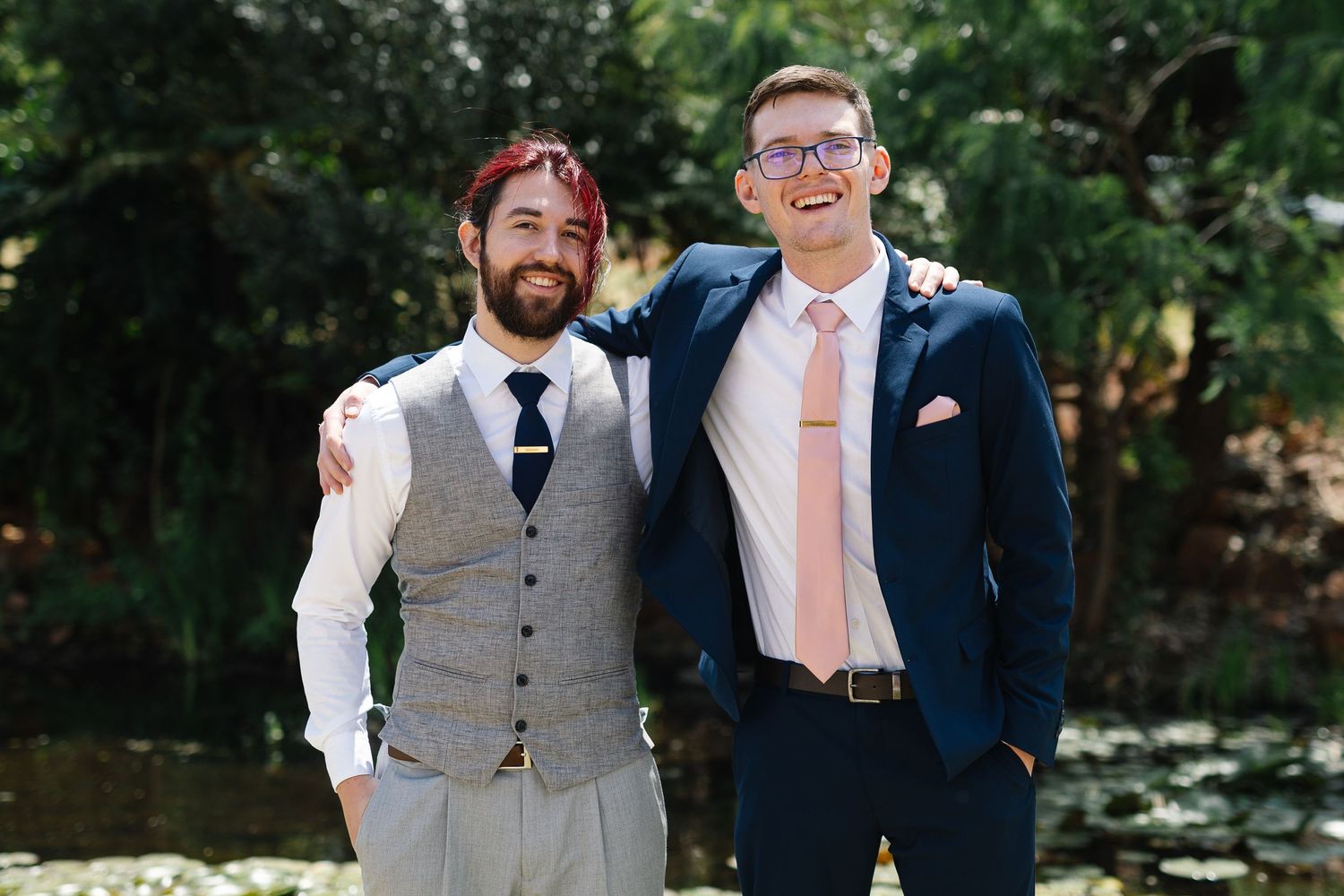Groomsmen in gray vests and navy suits share a candid moment together at an outdoor wedding celebration.