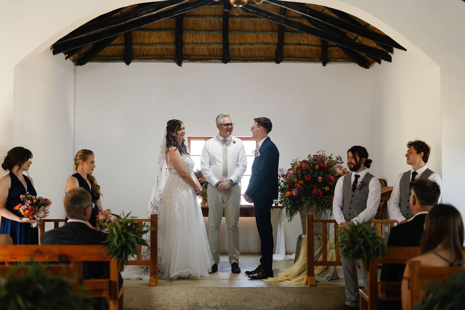 Wedding ceremony takes place in a rustic chapel with wooden beams and floral arrangements.