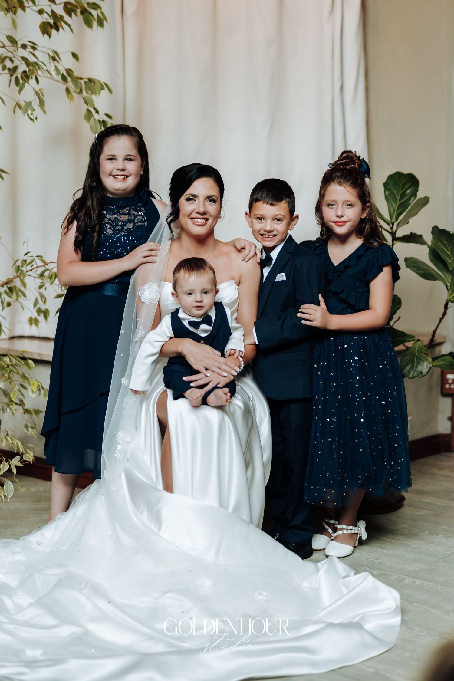 Beautiful bride in white gown seated with four children dressed in navy at an elegant wedding venue.