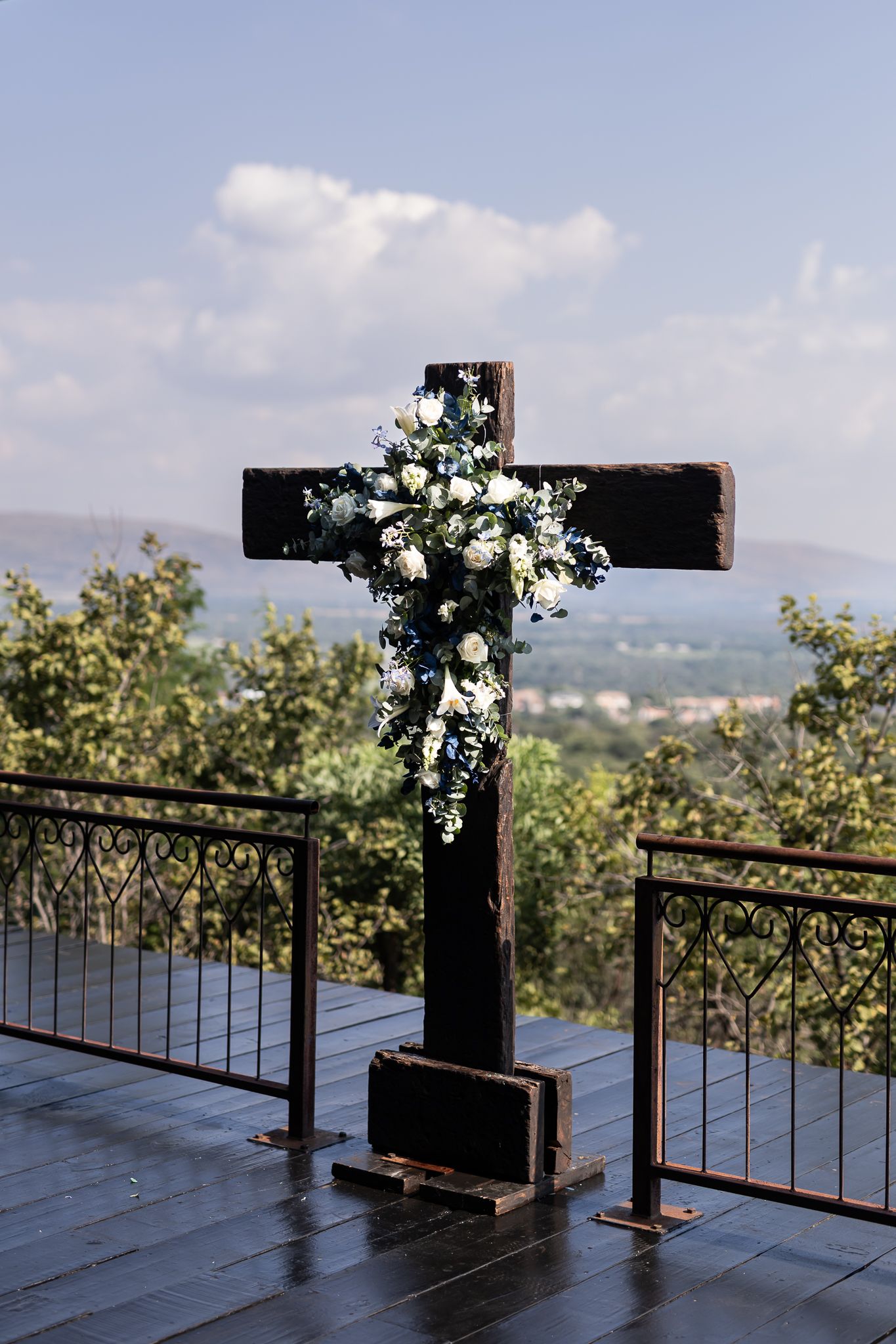 Large wooden cross decorated with white flowers against scenic mountain backdrop.