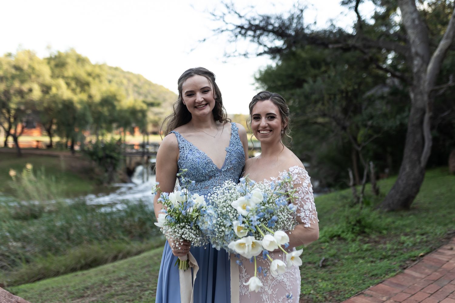 Wedding attendants pose with bouquets against scenic lake backdrop during outdoor celebration.