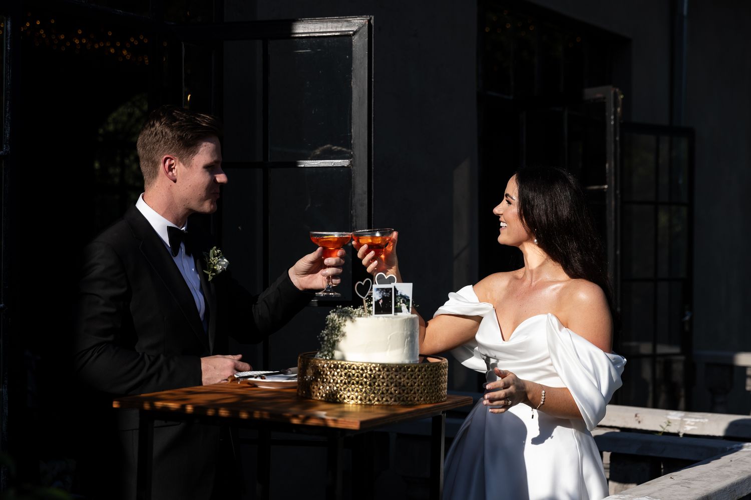 A couple shares a sweet moment while cutting their wedding cake at an outdoor venue.