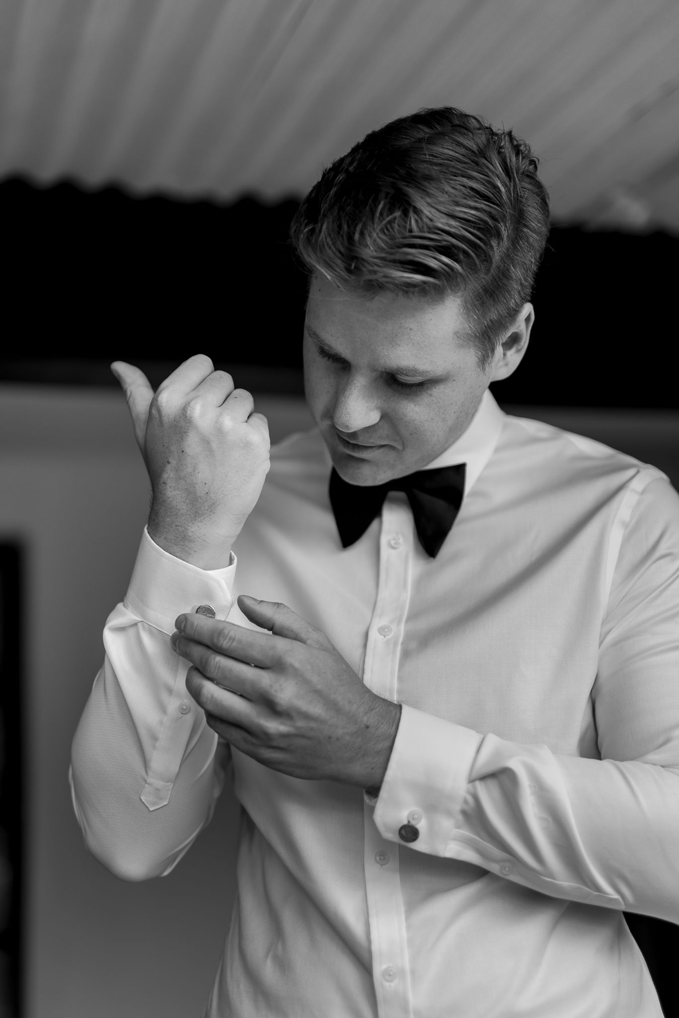 Person adjusting black bow tie while wearing crisp white formal shirt.