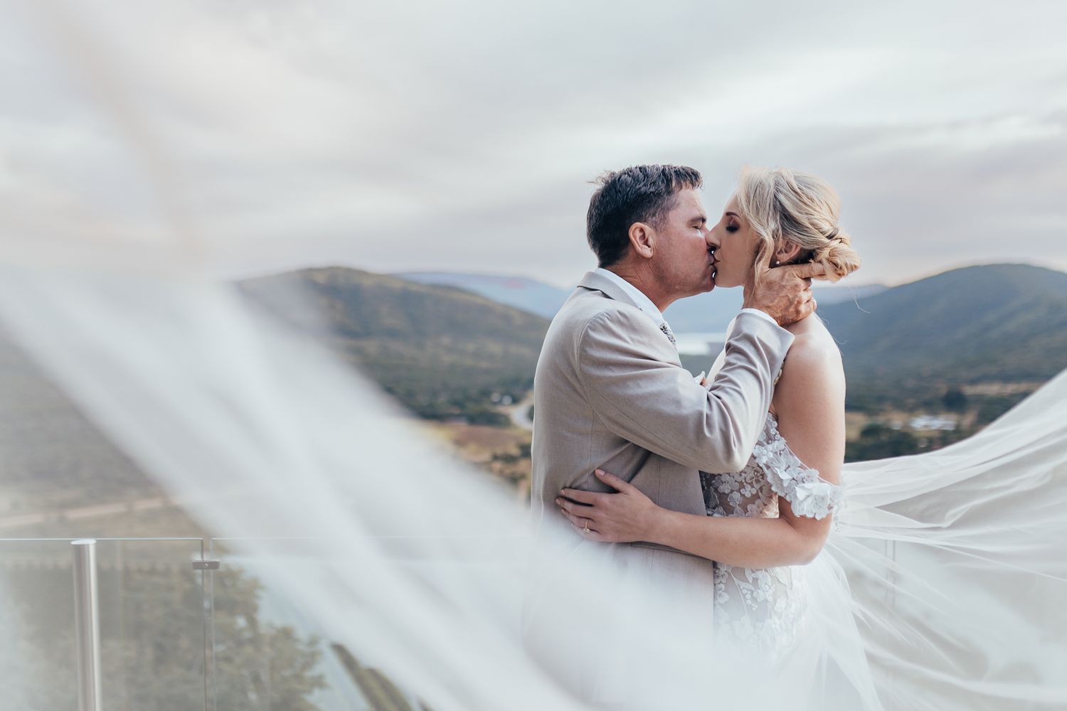 Intimate wedding portrait with flowing veil against scenic mountain backdrop.