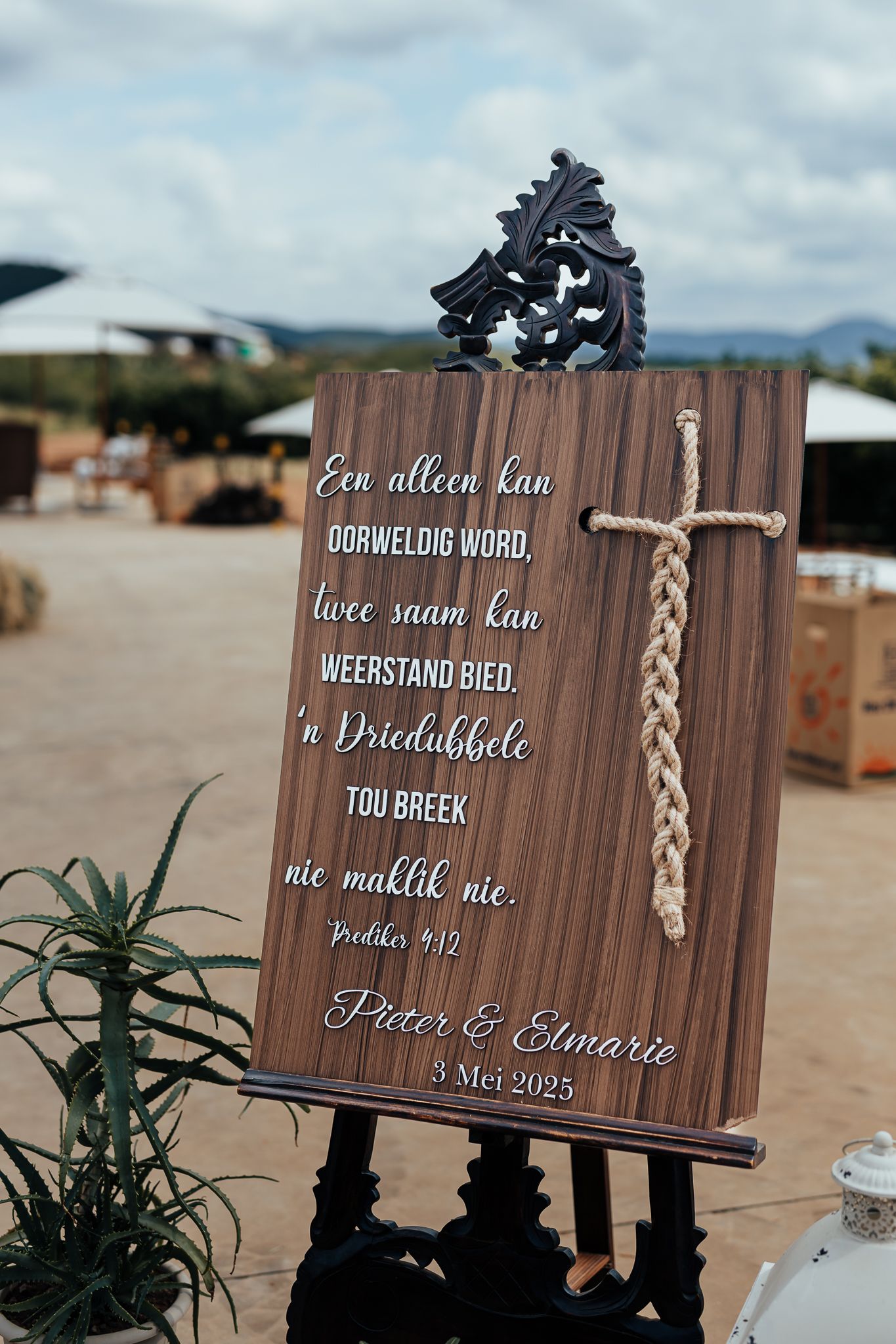 A rustic wooden wedding sign with text in Afrikaans displayed on an ornate easel.