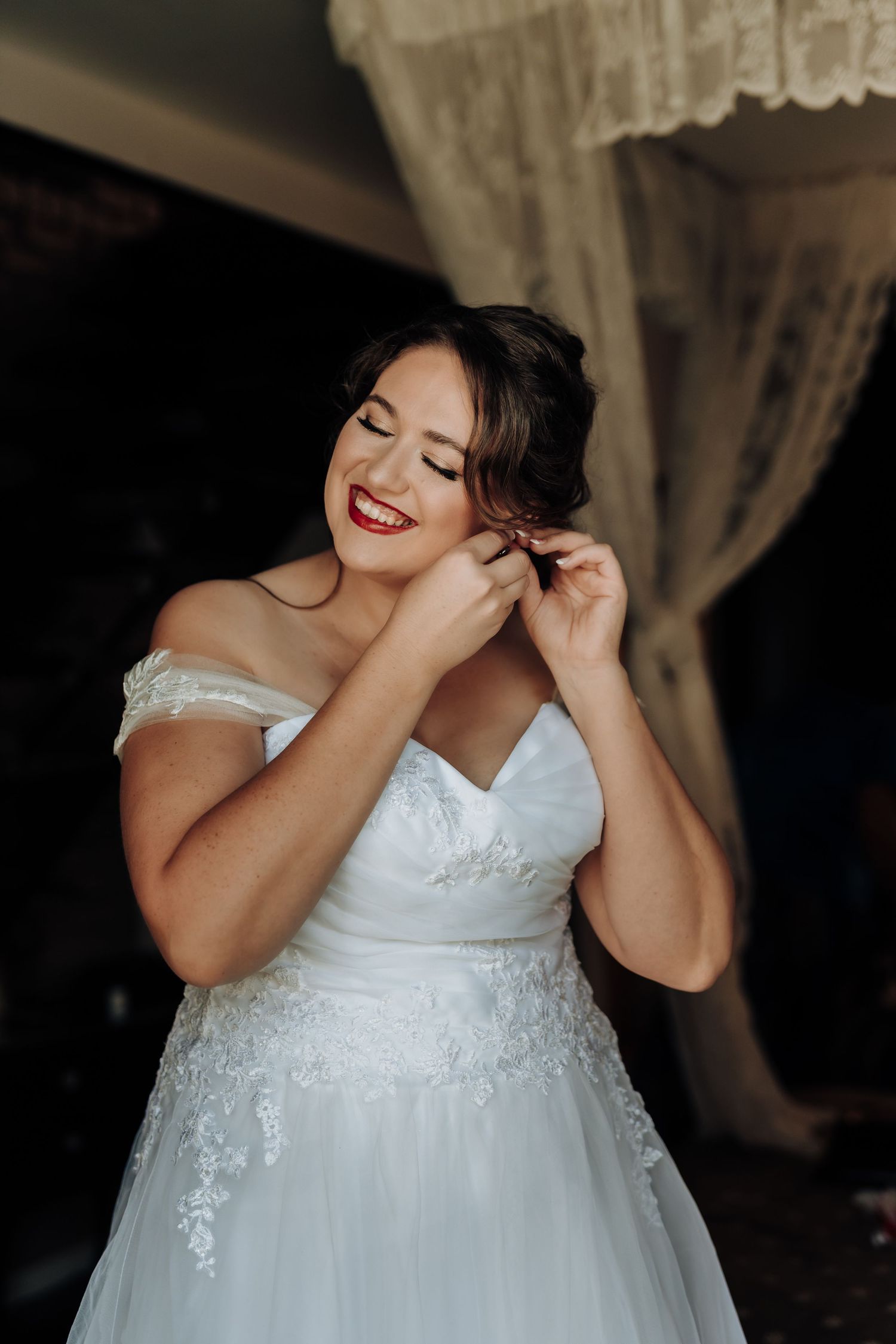Candid moment of a bride laughing while putting on jewelry.