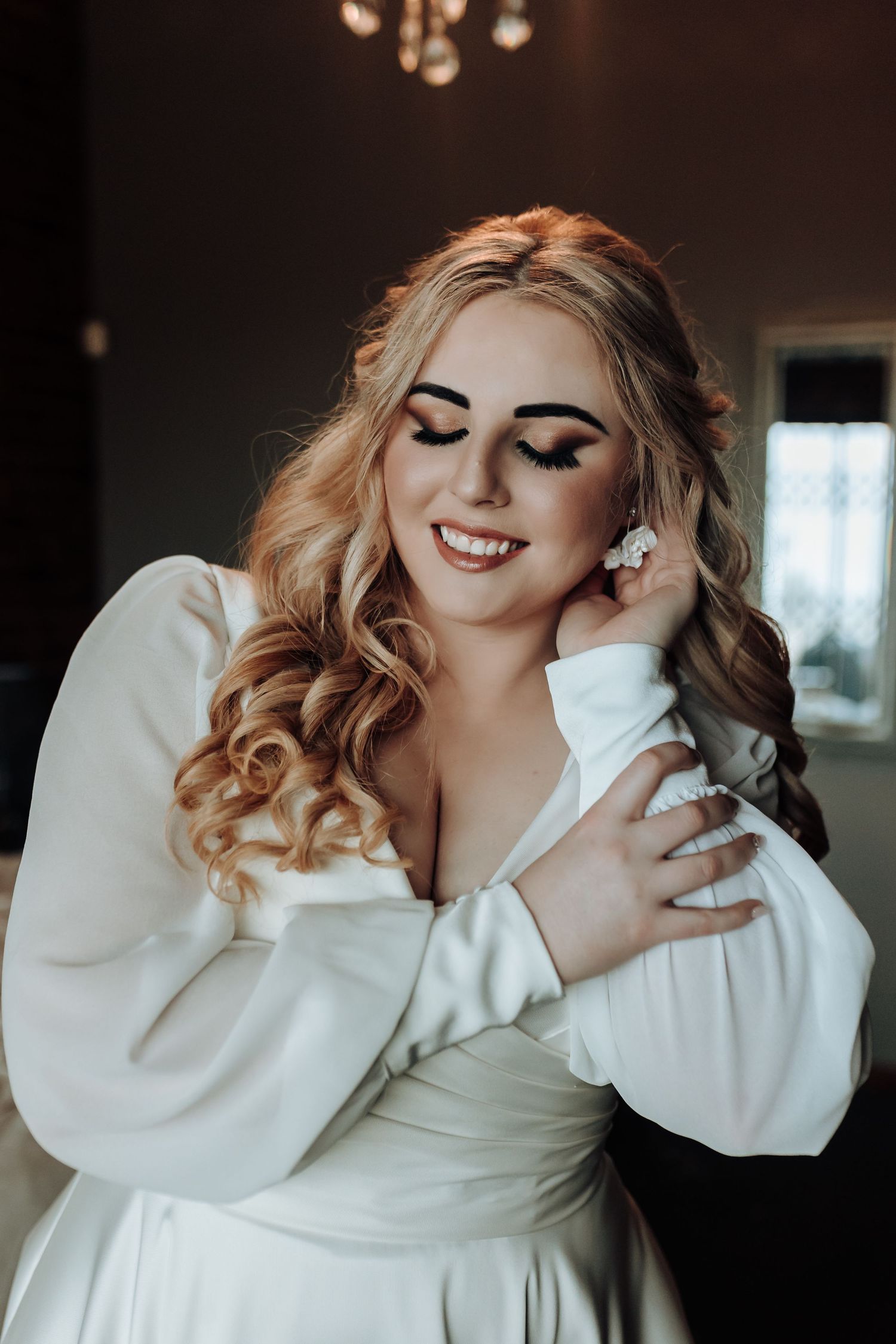 An intimate portrait showing elegant makeup and styled blonde curls with a white dress.
