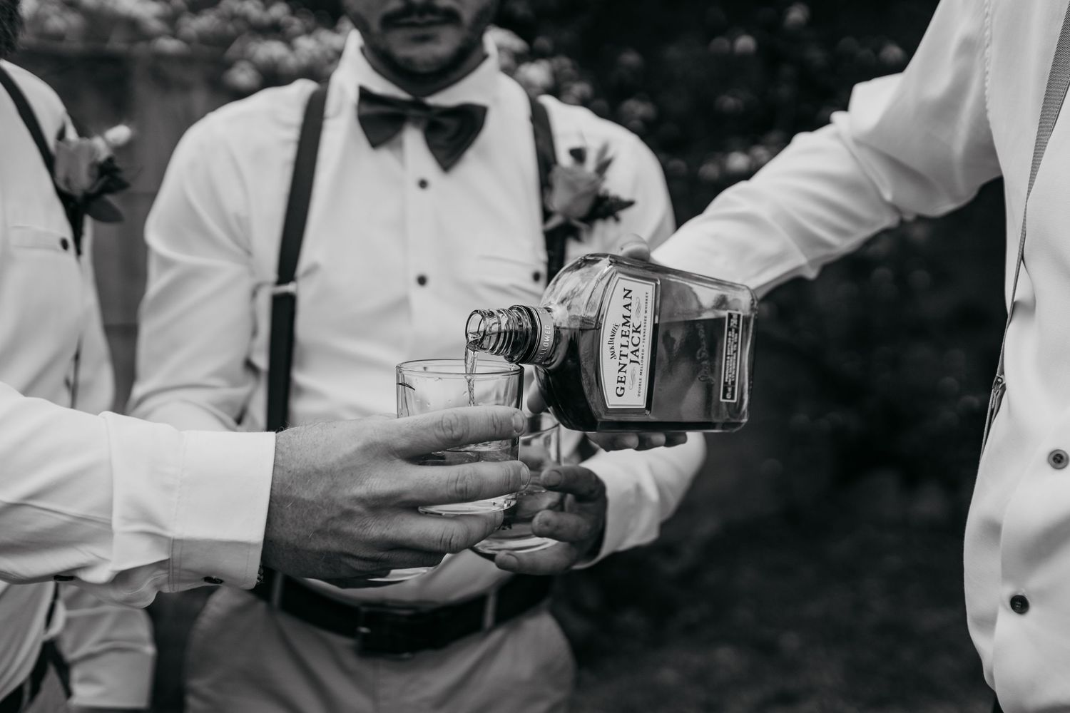 Close up of hands pouring drinks into glasses at outdoor wedding celebration.