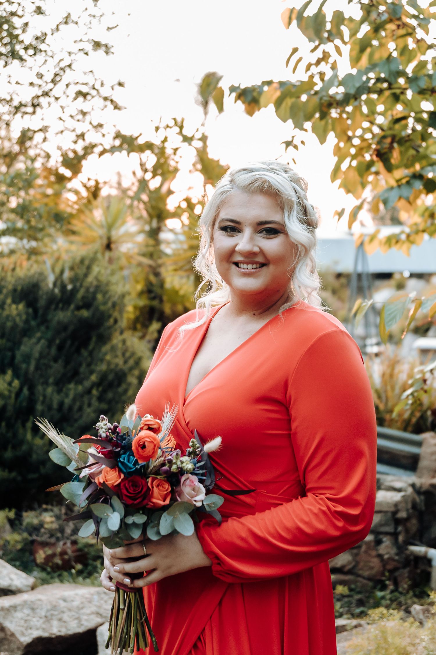 Bridesmaid in coral dress holds vibrant floral bouquet in garden setting.