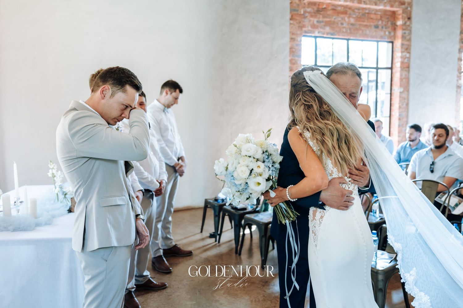 An emotional wedding ceremony moment in a bright industrial venue with brick walls and white decor.