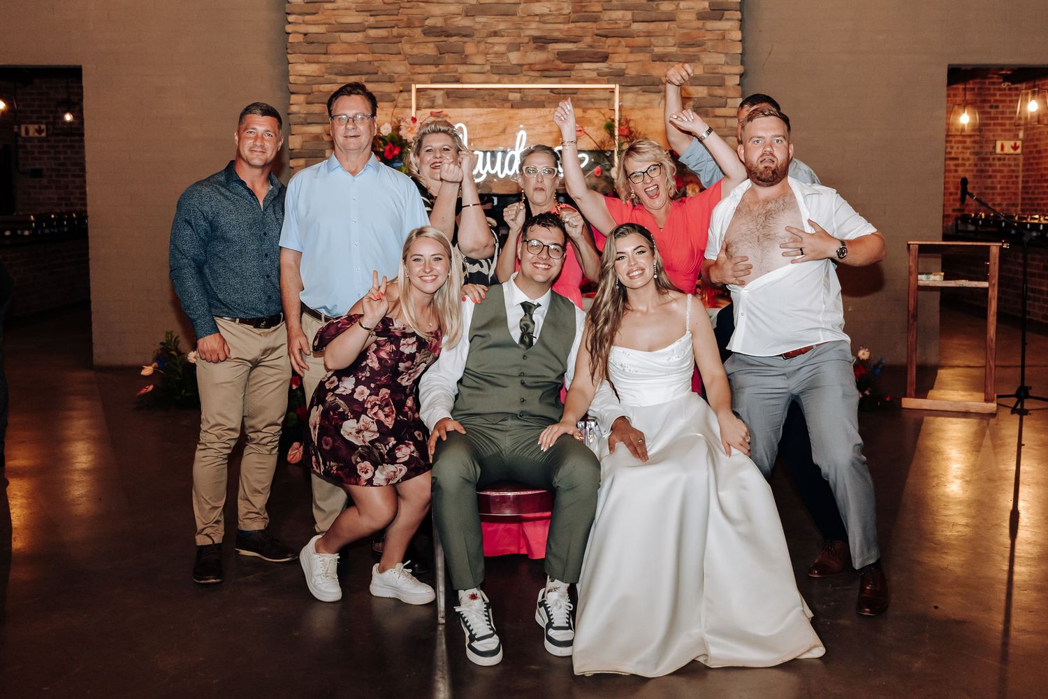 Wedding party poses together for a celebratory group photo in a rustic venue.
