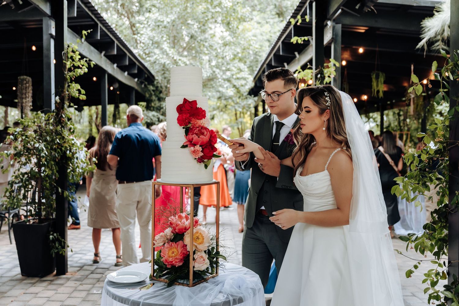 Wedding guests dance and celebrate at an outdoor reception with string lights overhead and floral decorations.