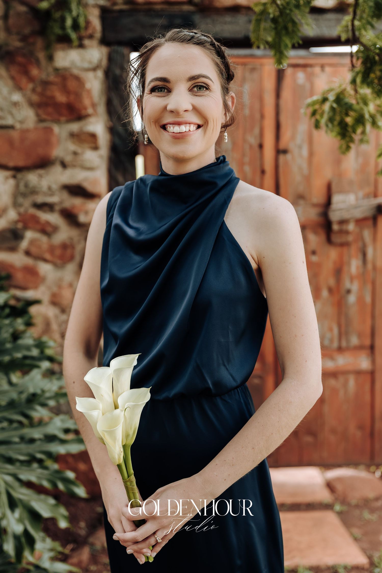A series of portraits showing someone in a navy blue sleeveless top holding a white calla lily against a brick backdrop.
