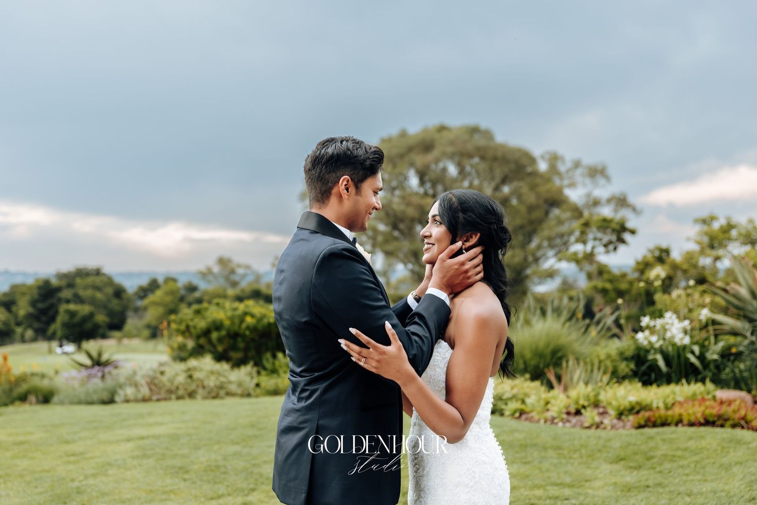 Couple embracing outdoors on grassy hill with trees in background.