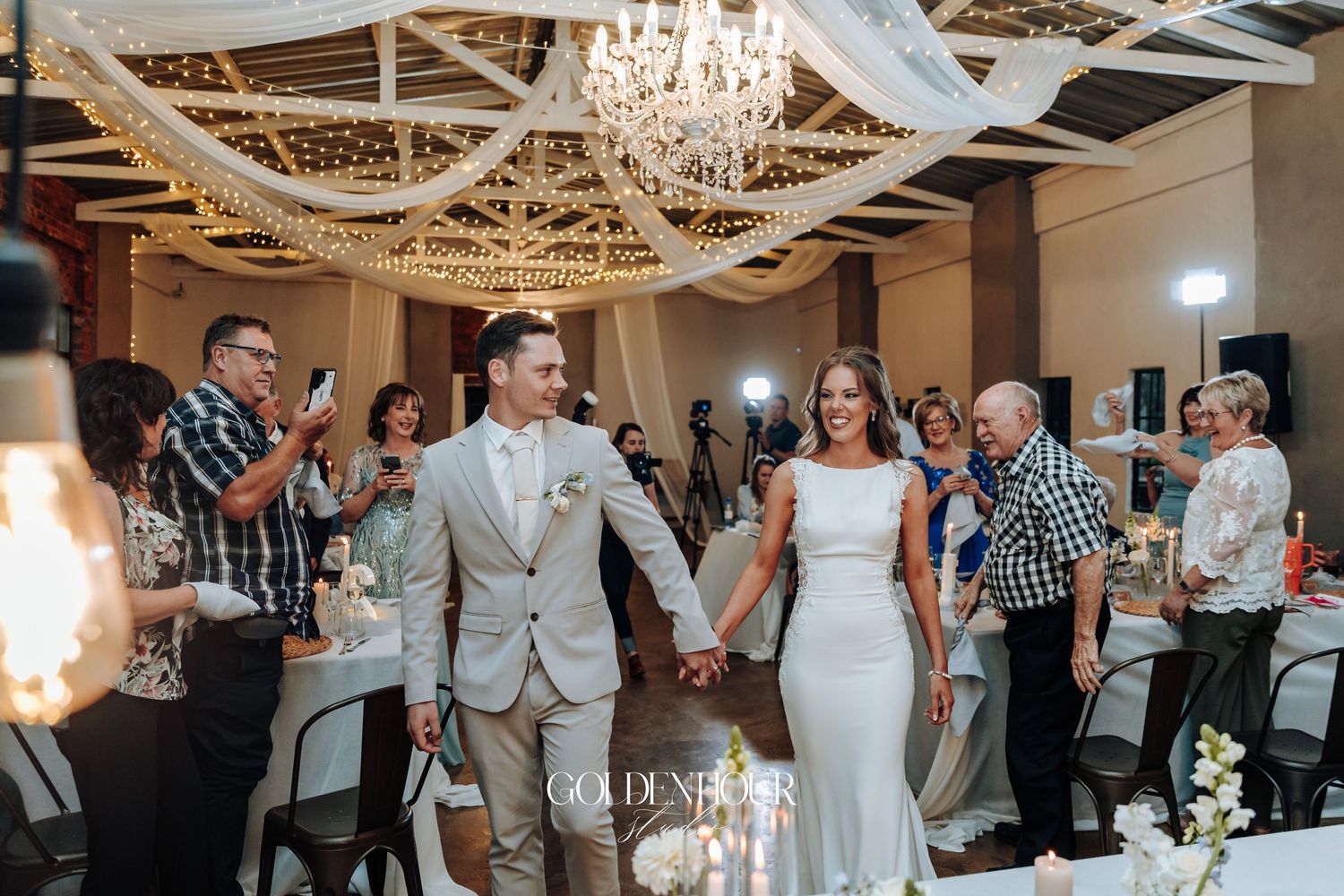 Wedding reception celebration in an elegant venue with chandelier and draped fabric ceiling decorations.
