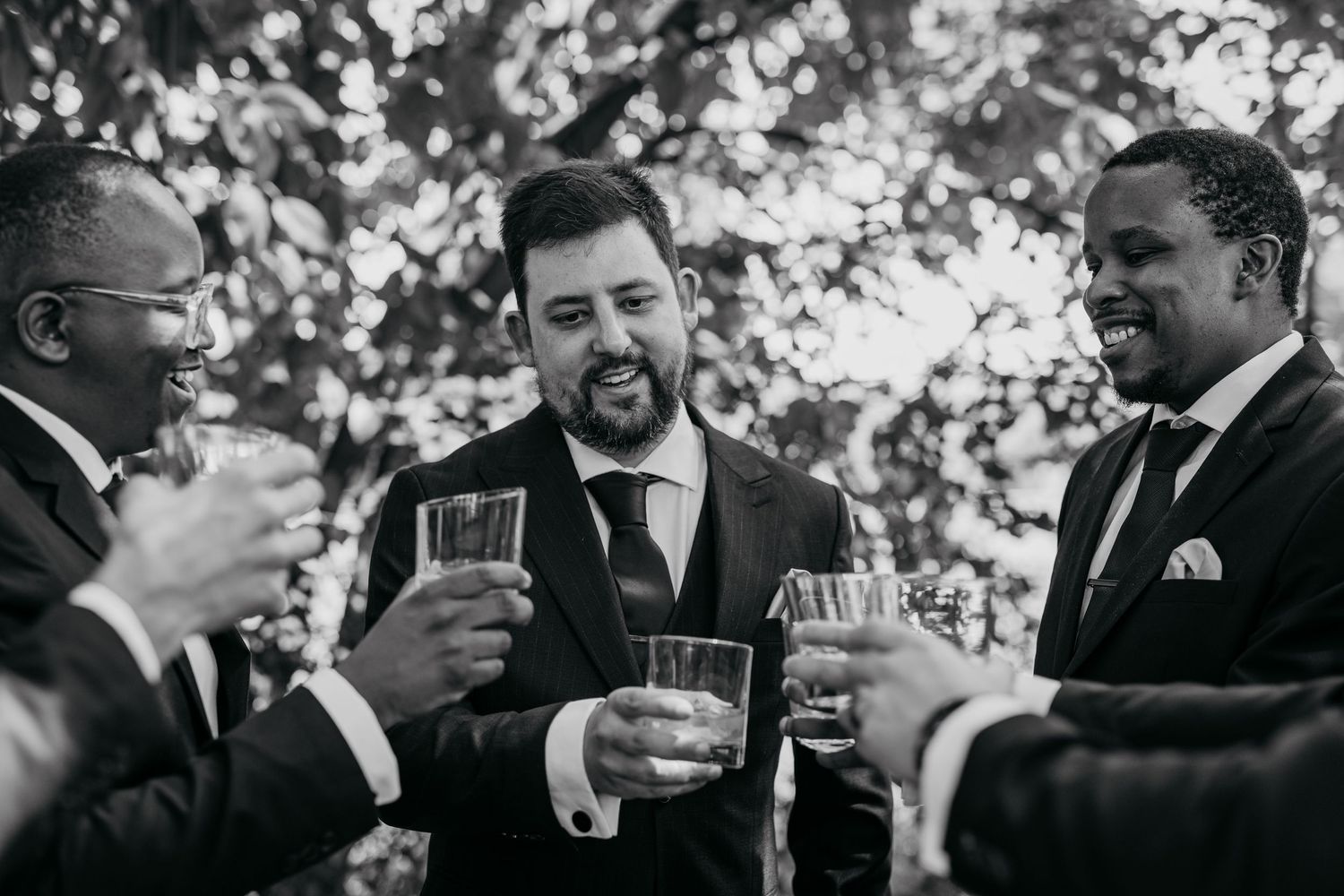 Groomsmen in suits share laughter and drinks during a wedding celebration.