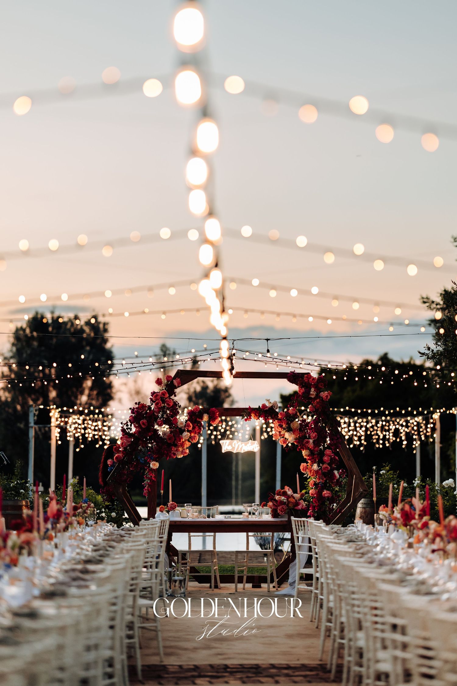 Outdoor wedding venue setup with rows of white chairs and string lights creating a romantic twilight atmosphere.