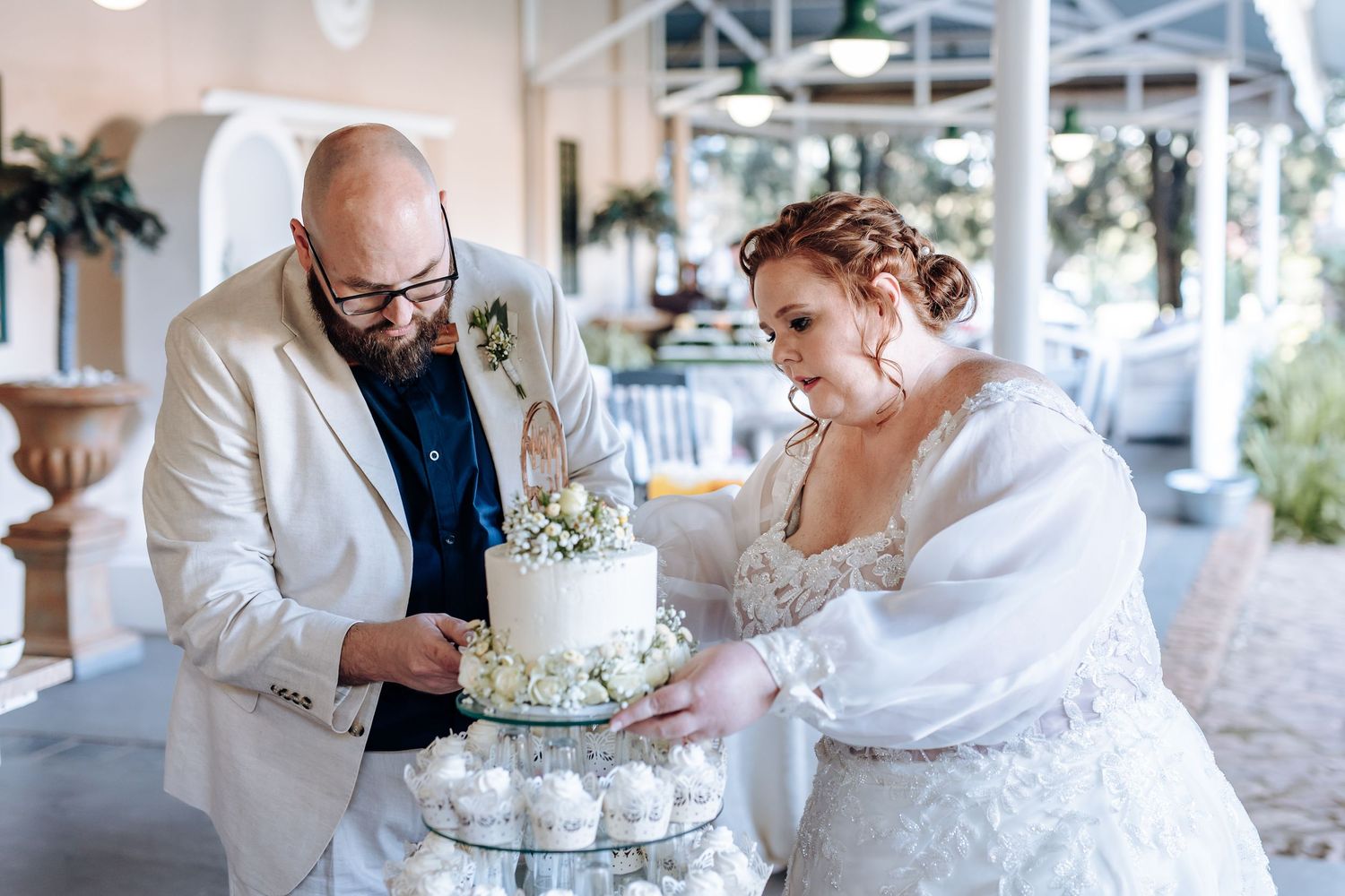 A wedding couple shares a bite of white tiered cake during their reception celebration.