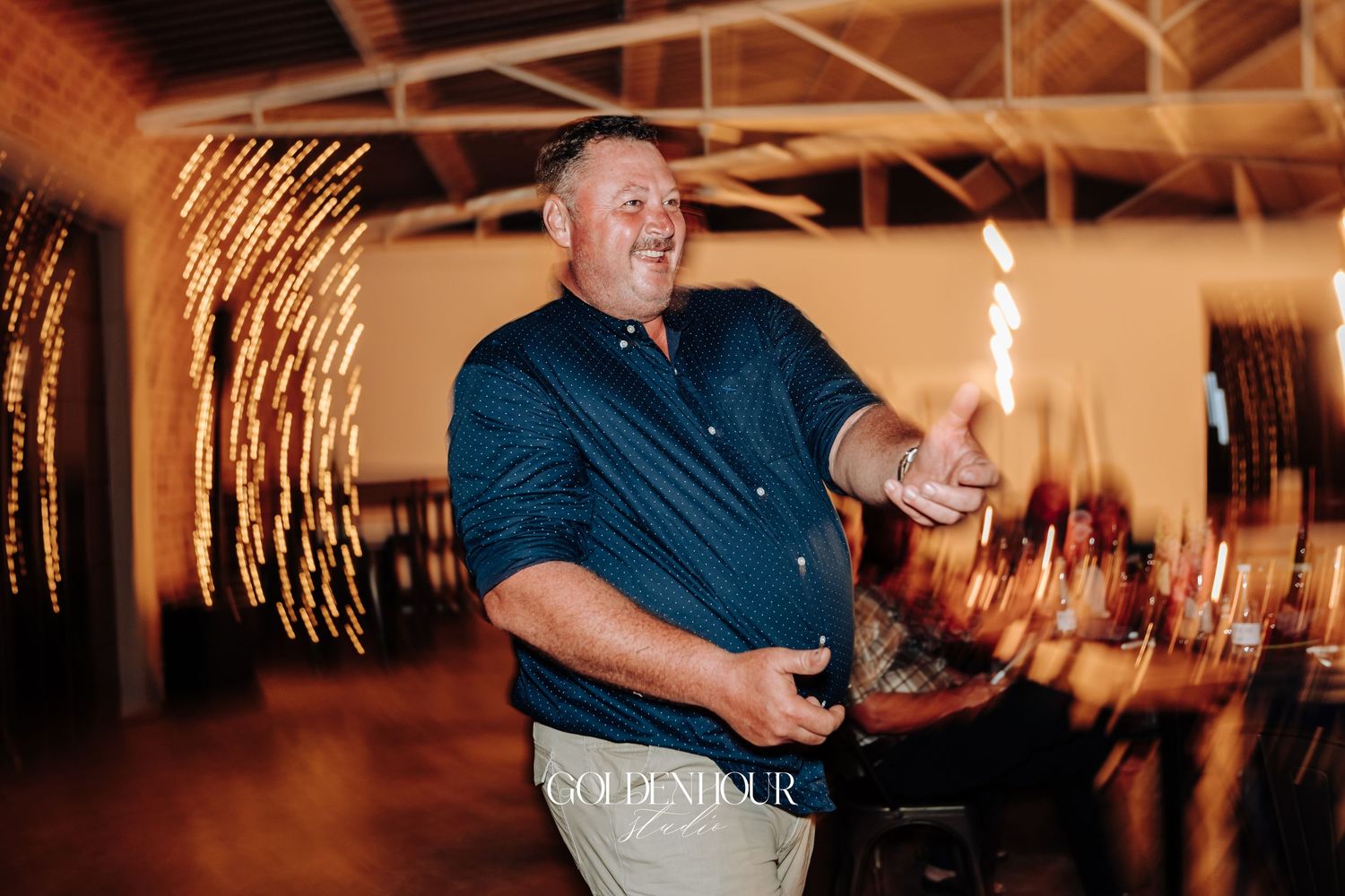 Joyful wedding guest in navy shirt celebrating with sparklers during festive indoor reception party.