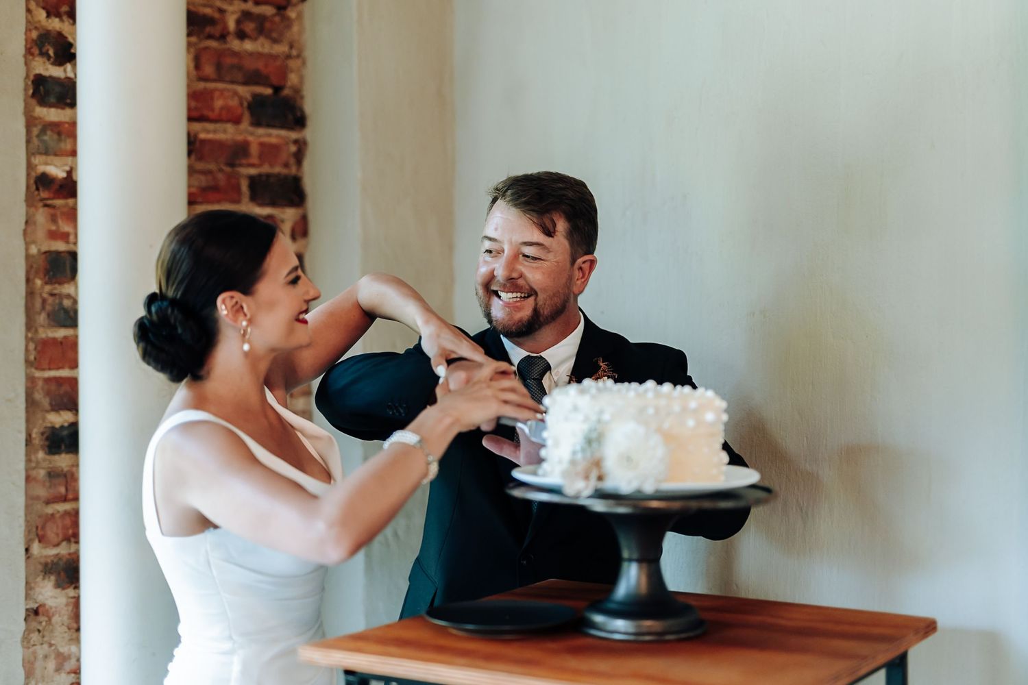 A couple shares a slice of wedding cake together during their reception celebration at a rustic venue.