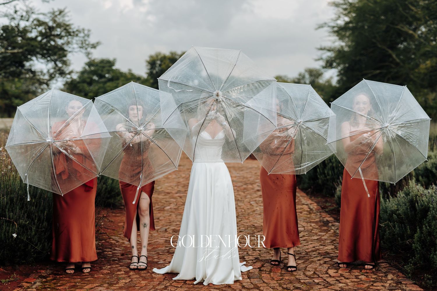 Wedding party holding clear umbrellas outdoors with coral colored dresses.