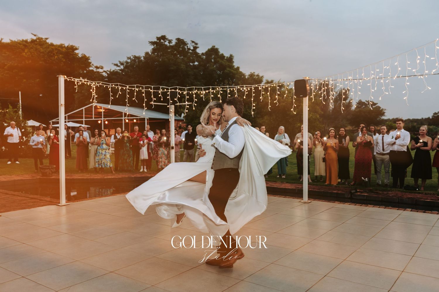 Outdoor wedding reception setup with string lights at sunset.