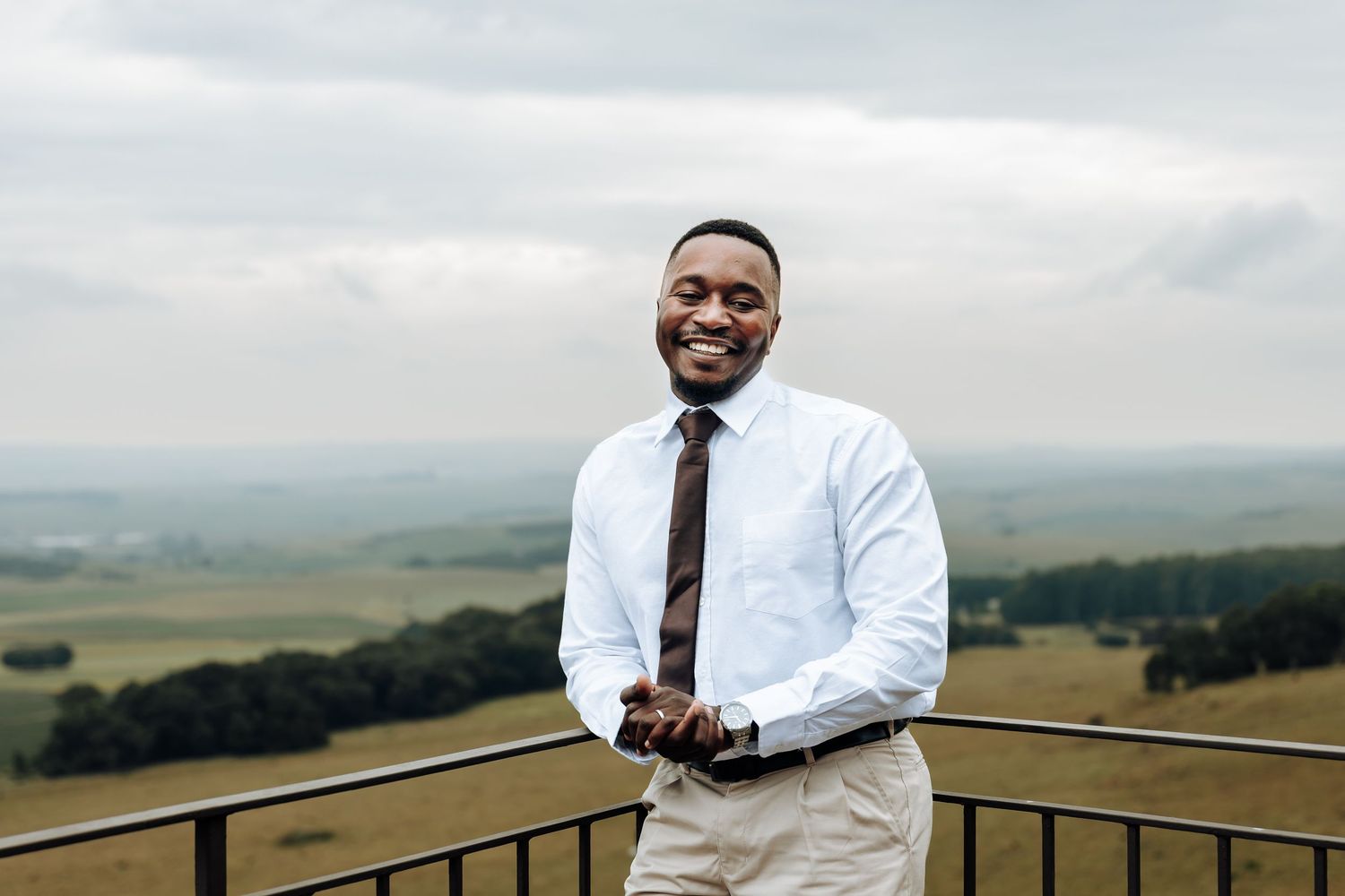 A professional in a white dress shirt stands on an outdoor viewing platform overlooking rolling green hills and countryside.