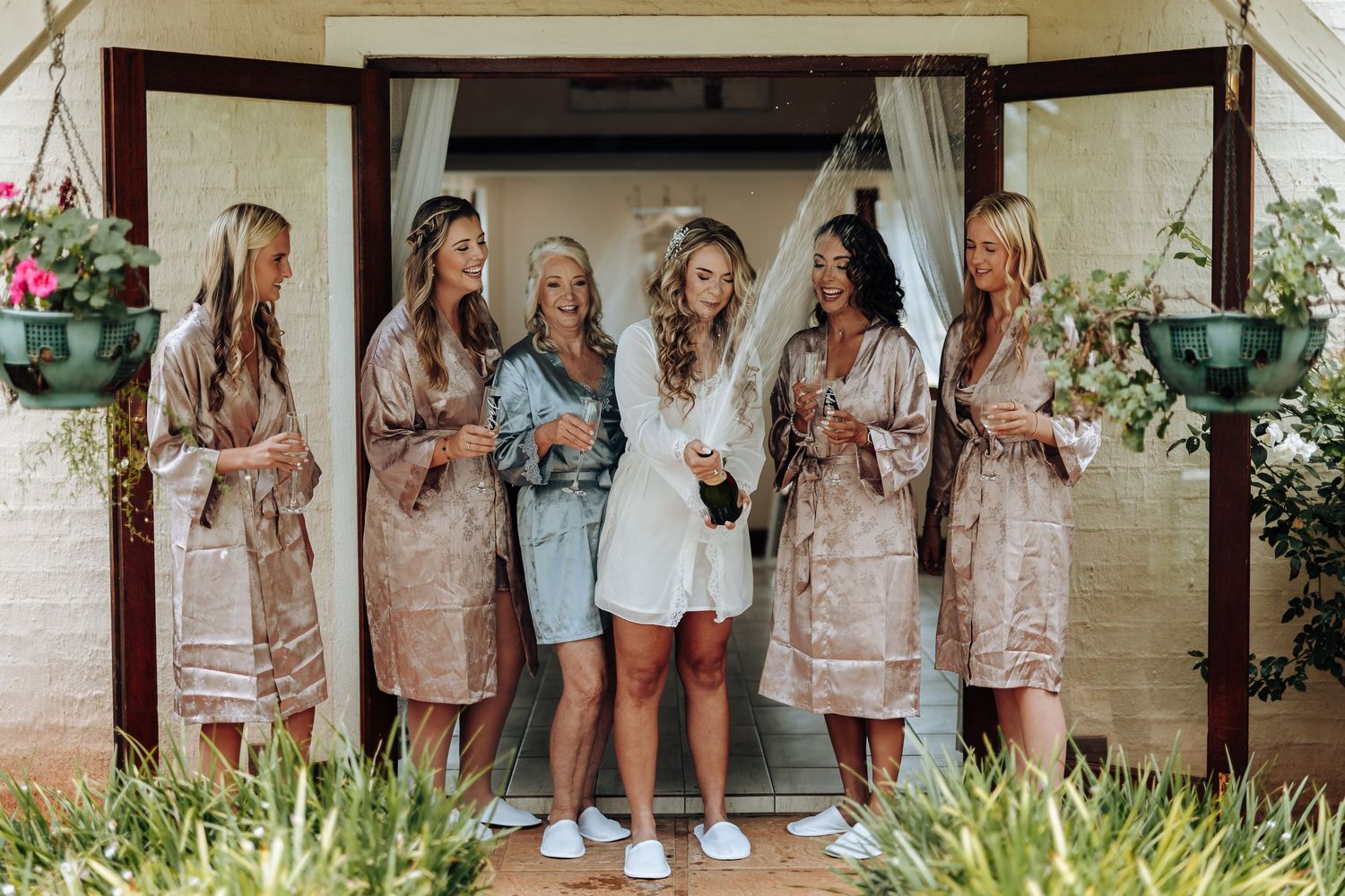 Group of people wearing coordinated neutral-toned outfits pose together in front of a white brick wall.