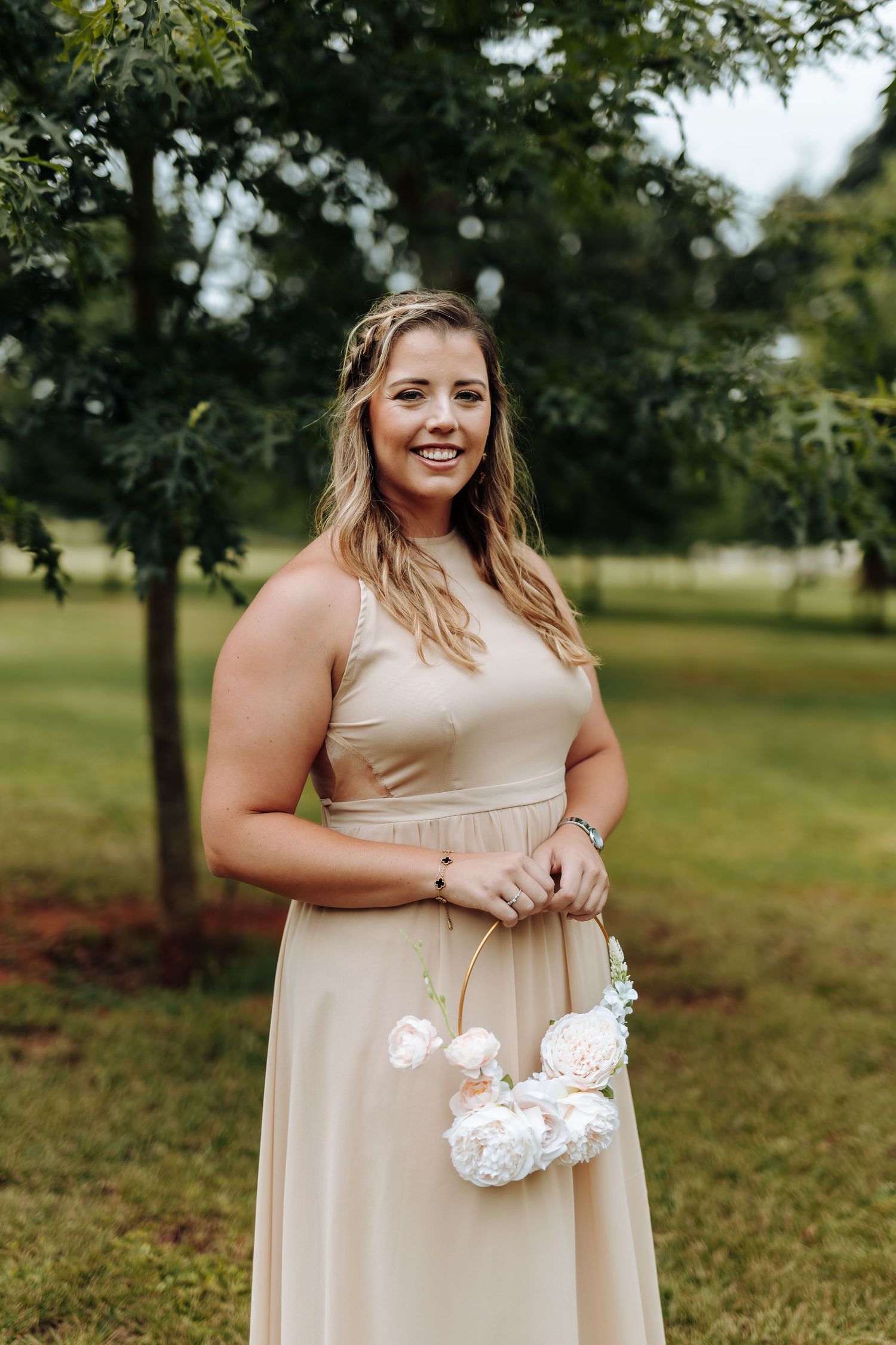 A person in a champagne-colored bridesmaid dress holds white flowers while standing in a grassy outdoor setting.
