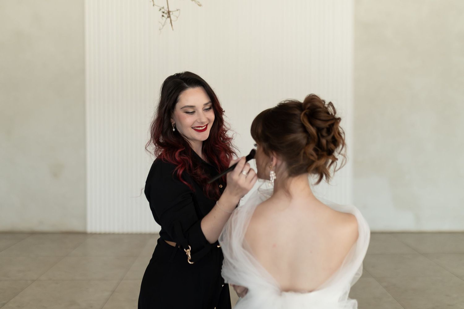 Stylist adjusts white wedding dress from behind while preparing for a photoshoot in a bright indoor space.