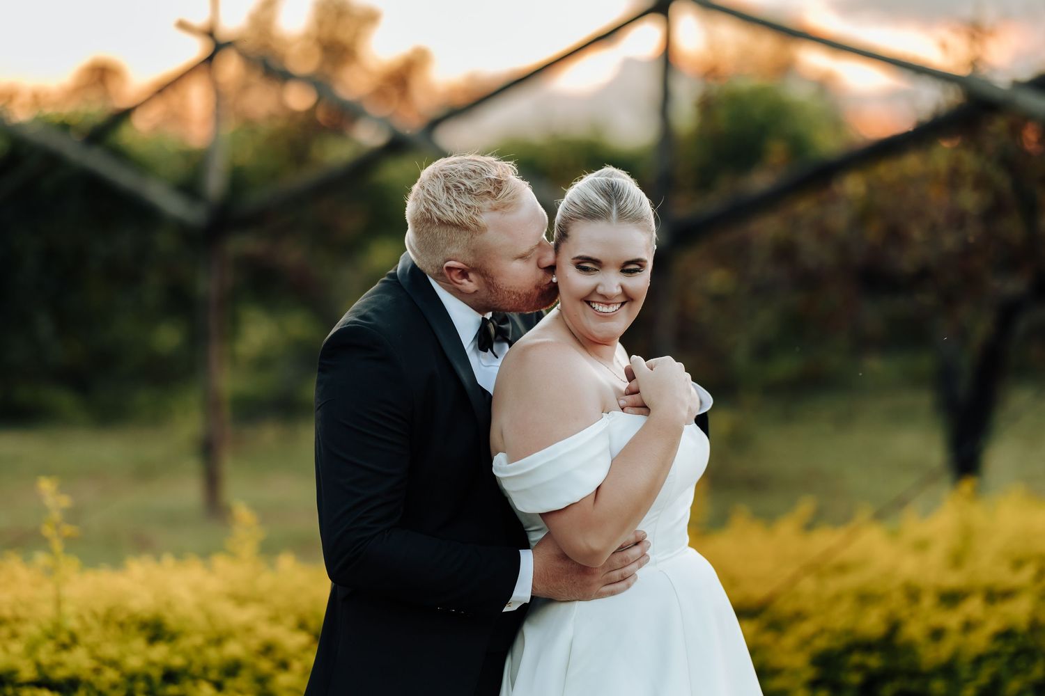 A couple in wedding attire shares joyful moments together during a golden sunset photo session.