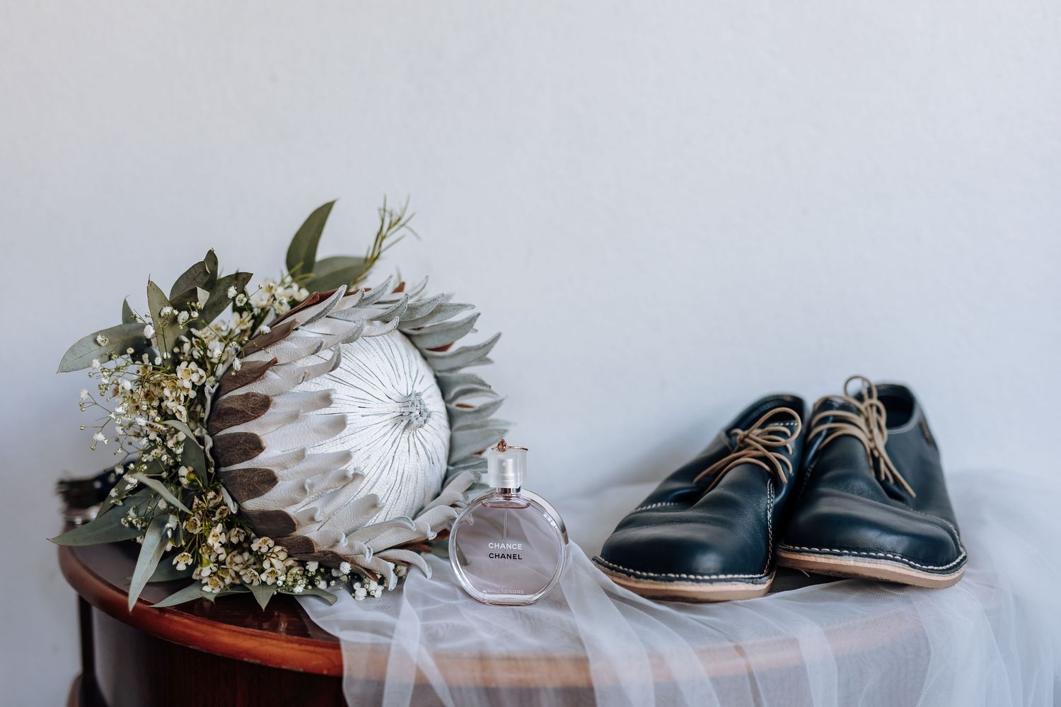 A collection of wedding shoes, floral arrangements, and bridal accessories arranged in a row against a light background.